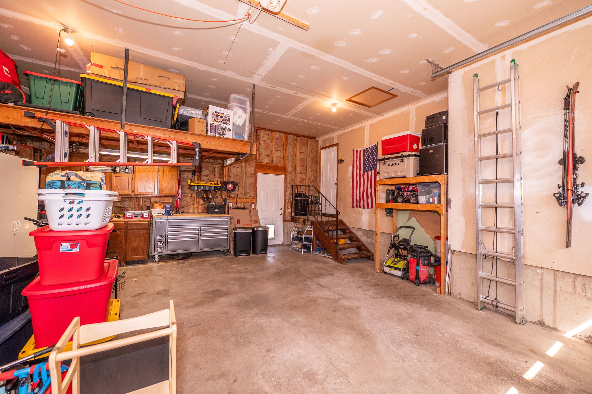 Spacious garage with concrete flooring, exposed ceiling joists, built-in shelving, wooden cabinetry, and a service door access point