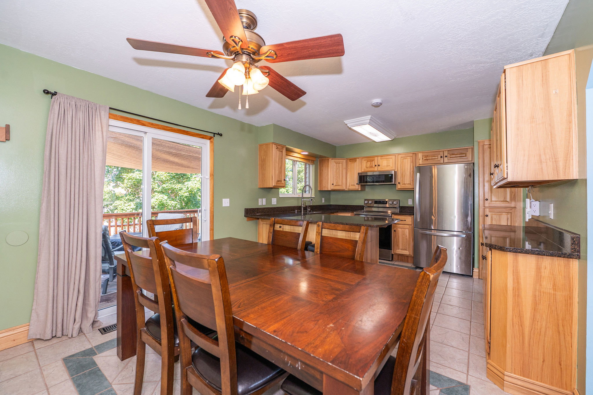 Kitchen and dining area featuring a sliding glass door, a ceiling fan, wood cabinetry, stainless steel appliances, and dark countertops