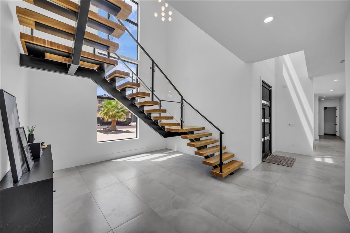 Open-concept entryway featuring a floating wood staircase with metal and glass railings, large format tile flooring, a multi-paneled entry door, and high ceilings with recessed lighting