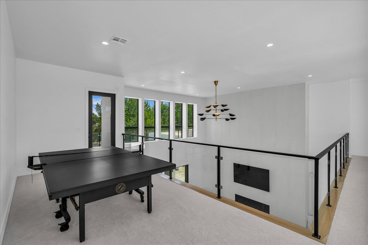 Open concept upper level featuring expansive windows, recessed lighting, a modern chandelier, and a glass panel railing system with black metal accents