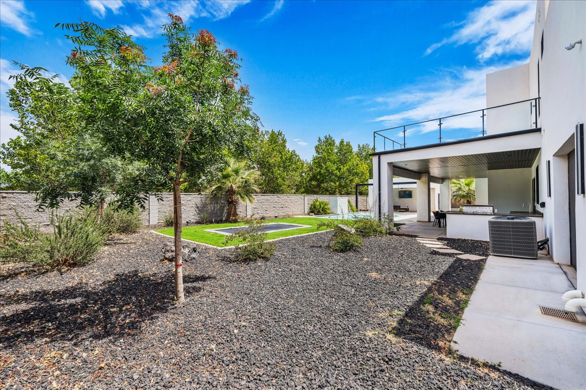 Expansive outdoor area featuring a modern covered patio with an outdoor kitchen, a second-story balcony with glass railings, a swimming pool, and a low-maintenance landscape with dark gravel and artificial turf