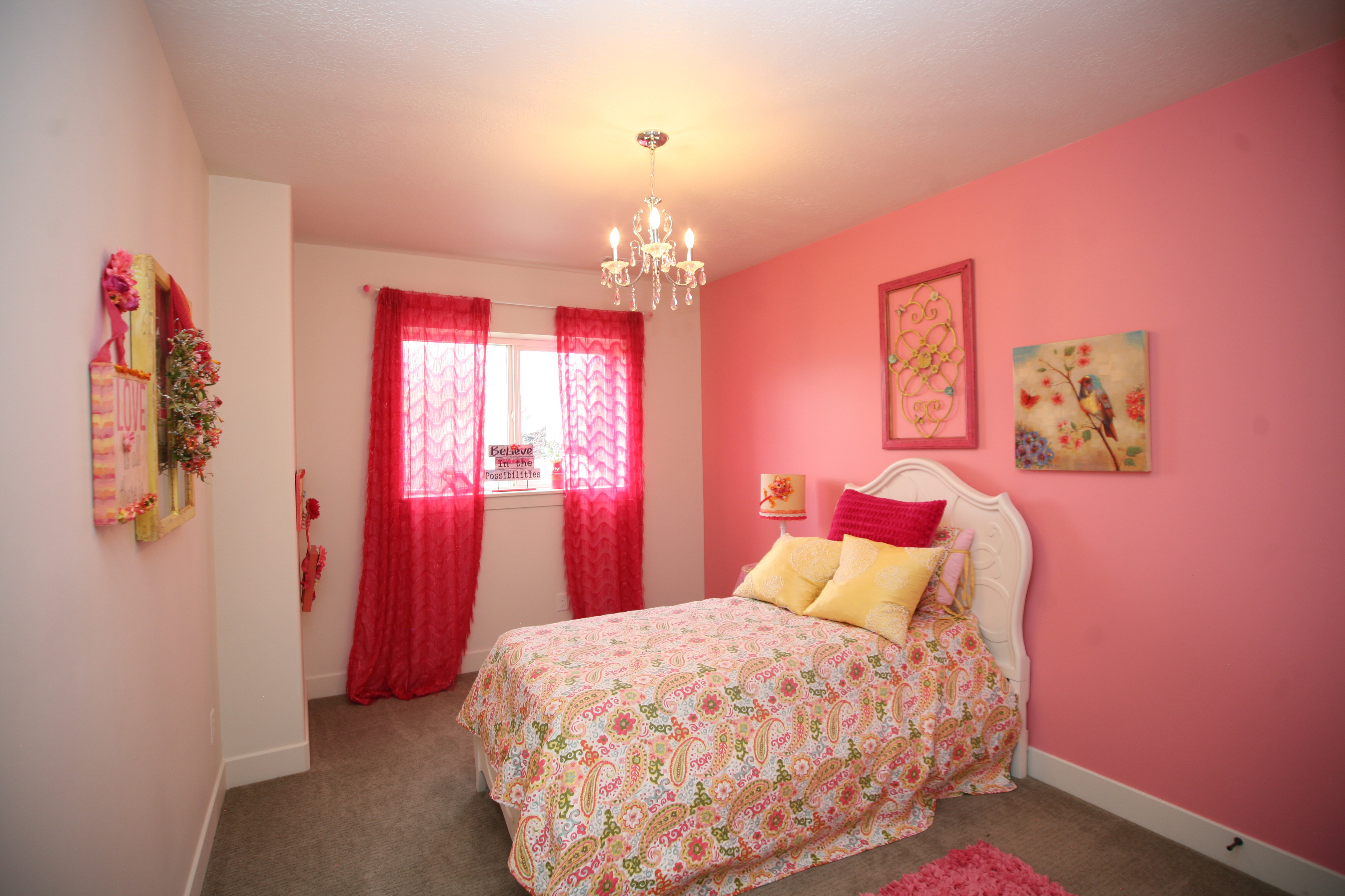 Daylight basement bedroom perfect for a little princess.  Carpeted room with a central window, white baseboards, and a ceiling-mounted chandelier light fixture