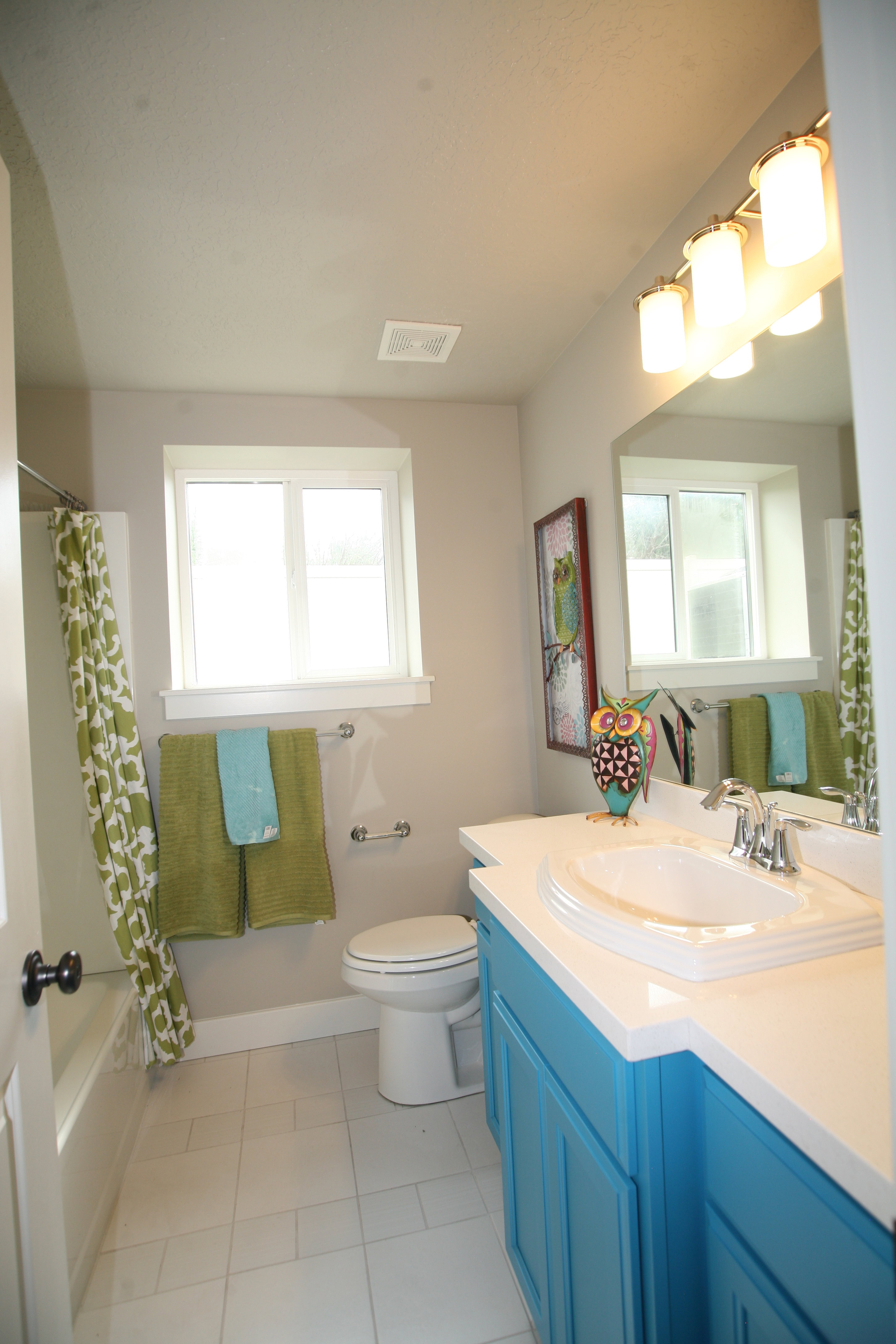 Bathroom featuring a single basin vanity with a white countertop and blue cabinetry, a white porcelain toilet, and a bathtub with a shower kit