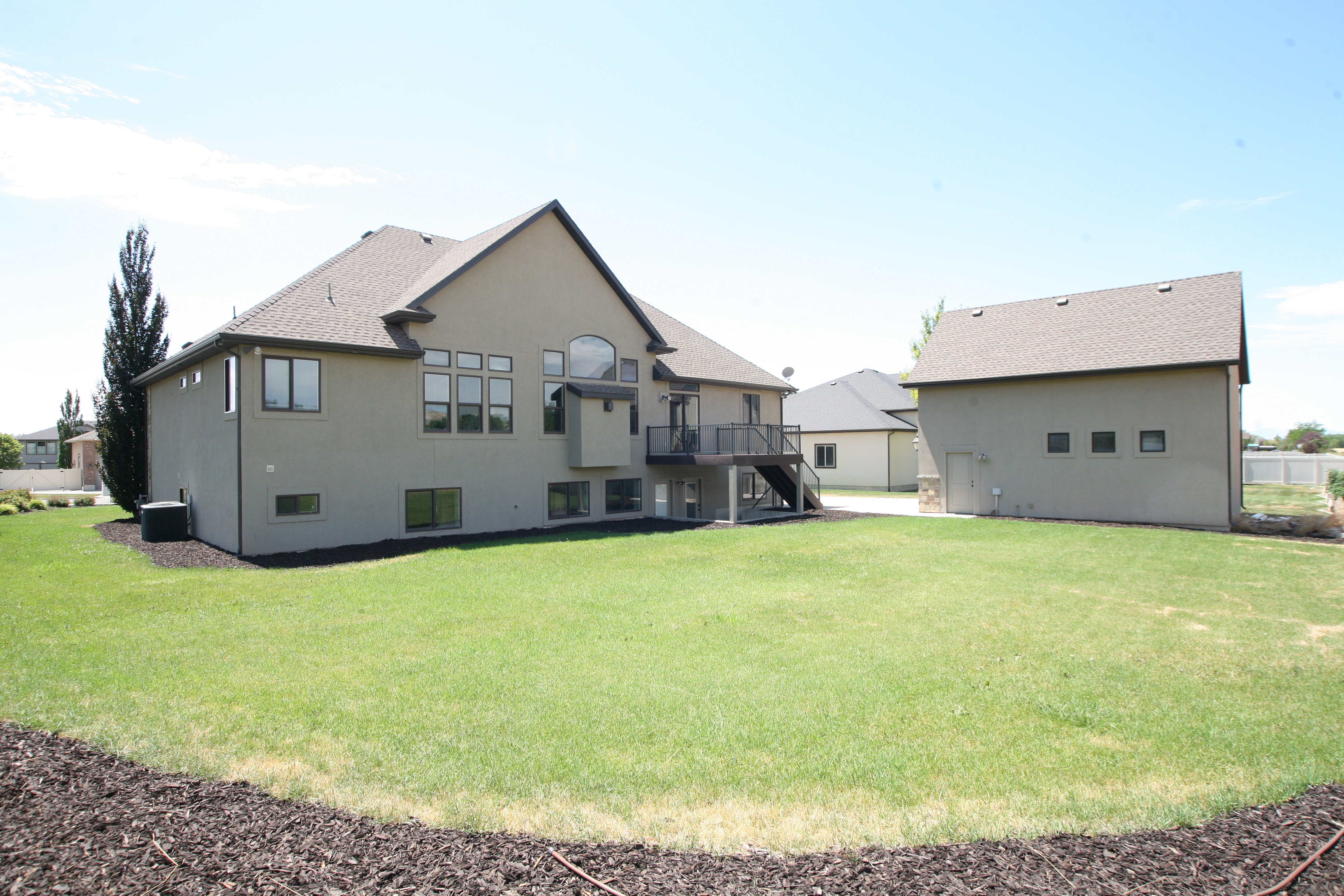 Expansive backyard featuring a manicured lawn, a multi-story residence with a stucco exterior, and a detached auxiliary building