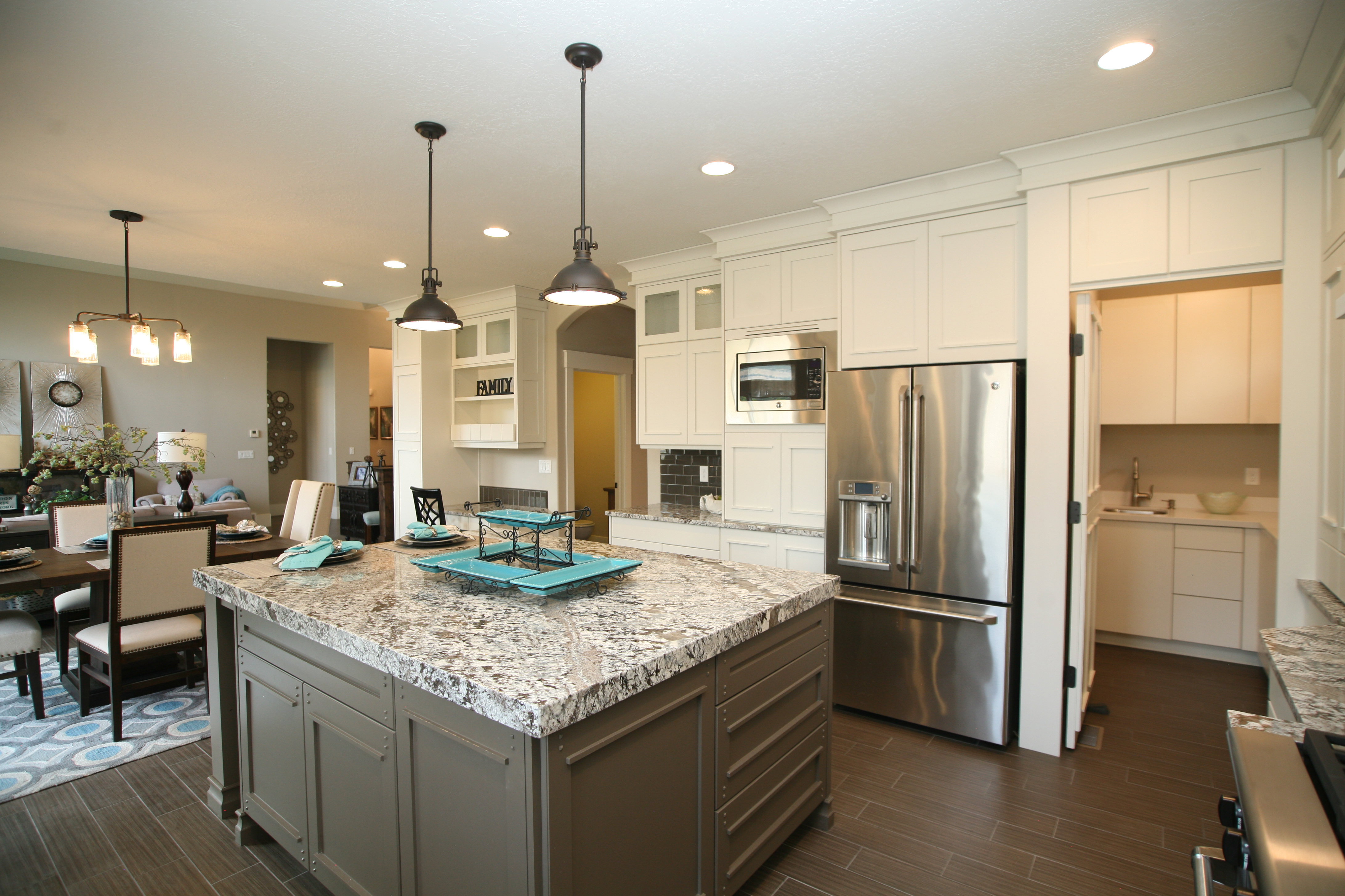 Spacious kitchen featuring a large central island with a granite-style countertop, pendant lighting, stainless steel appliances, white cabinetry, and wood-finish flooring