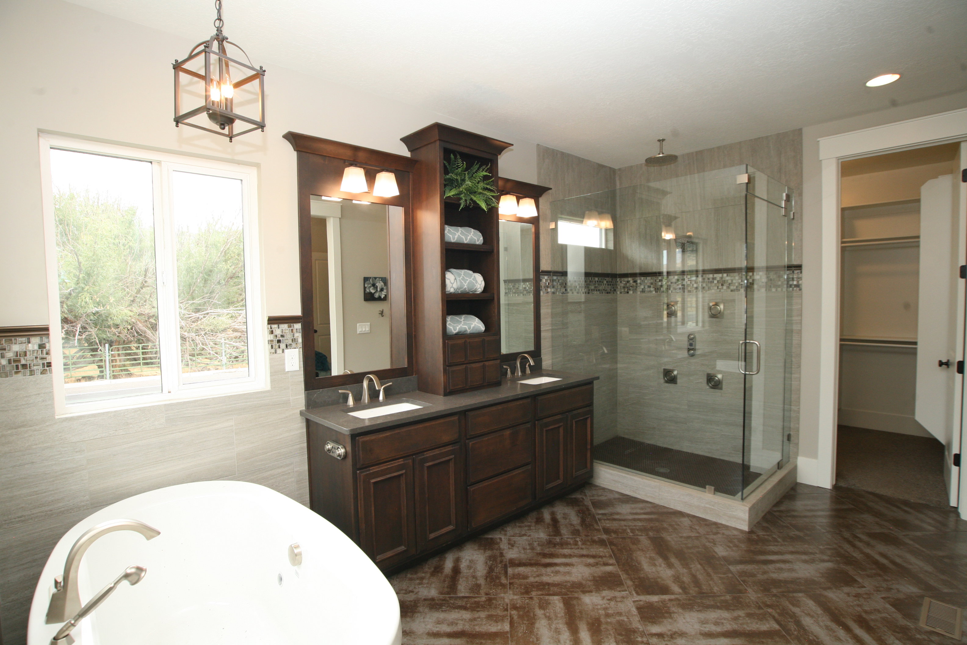 Spacious bathroom featuring a freestanding soaking tub, dual vanity with dark wood cabinetry, large glass-enclosed shower with multiple sprayers, and tile flooring