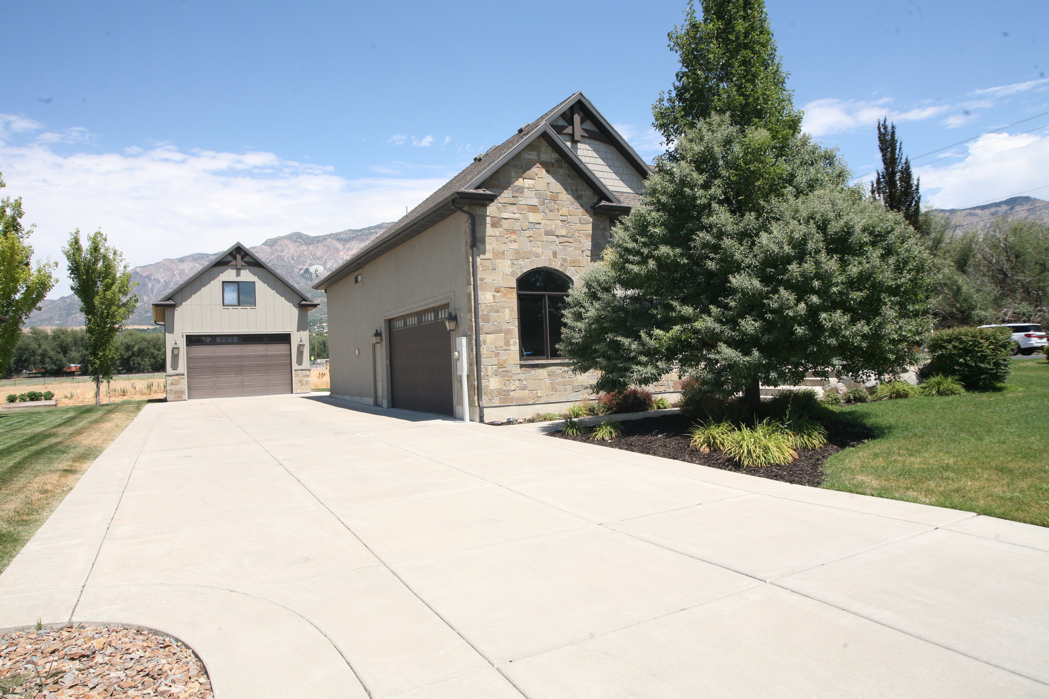 Expansive concrete driveway leading to a stone-clad exterior with a two-car garage