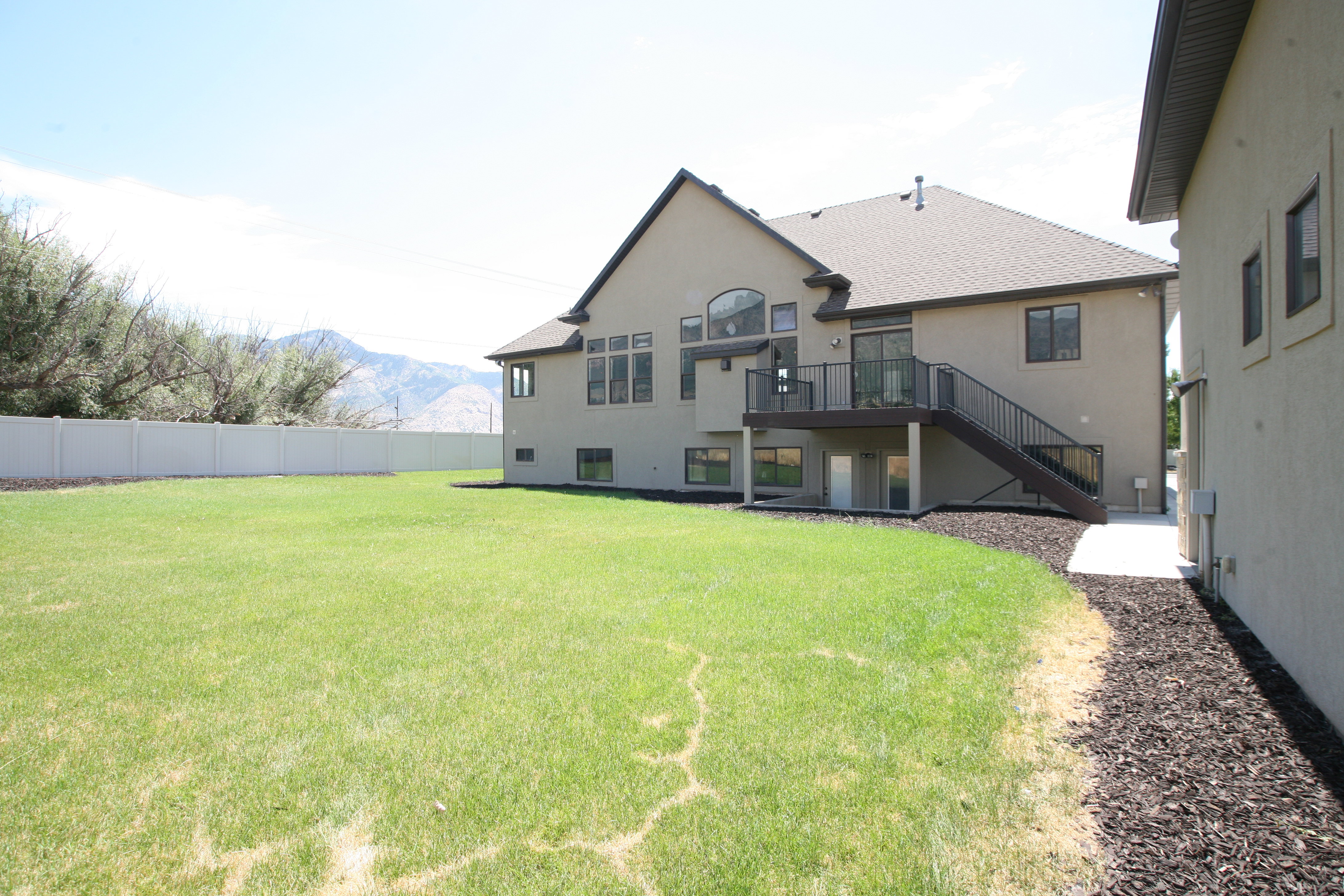Expansive backyard featuring a lush lawn, white vinyl fencing, and a mountain backdrop