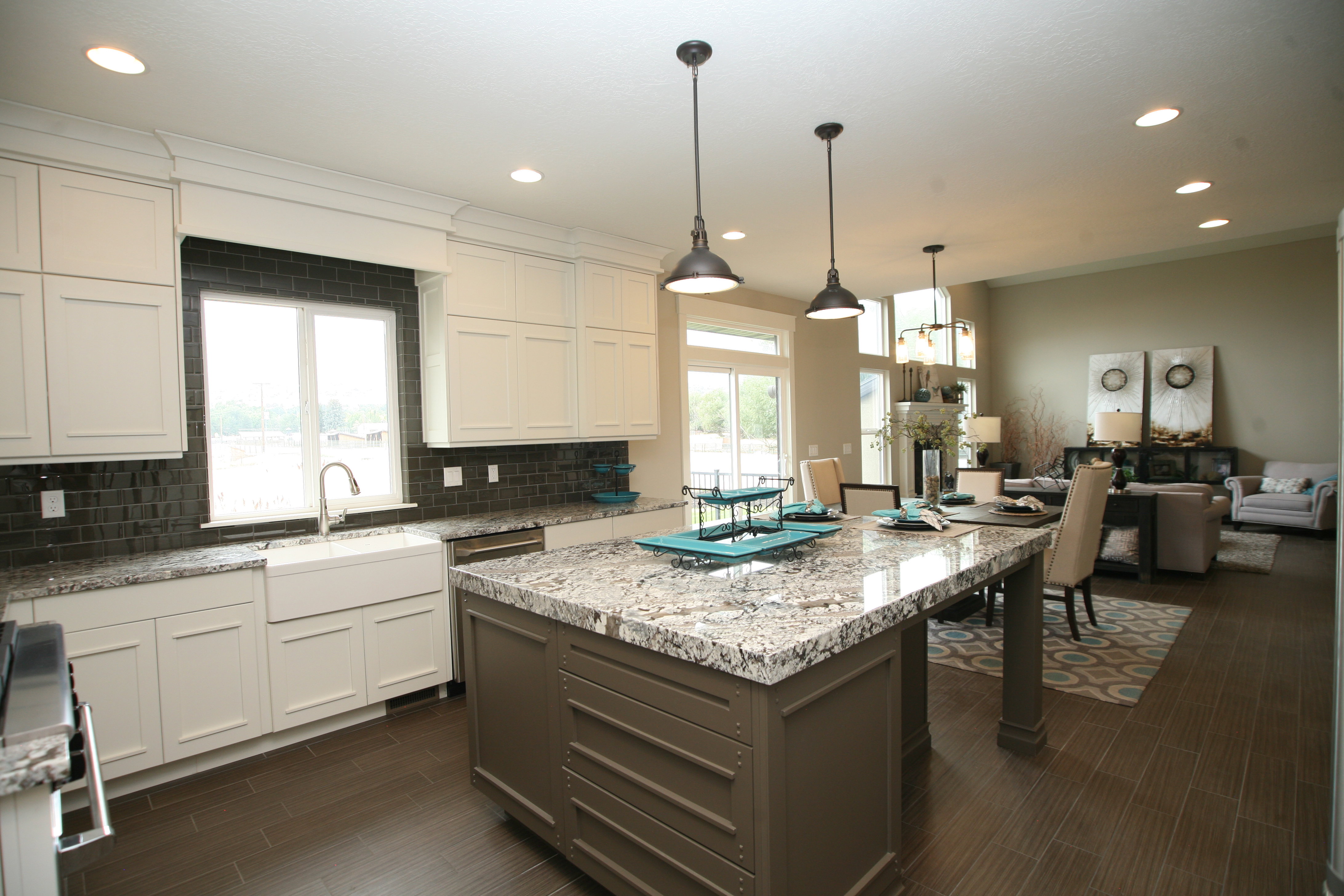 Gourmet kitchen featuring a large central island with granite countertops, white shaker-style cabinetry, a farmhouse sink, and a dark tile backsplash