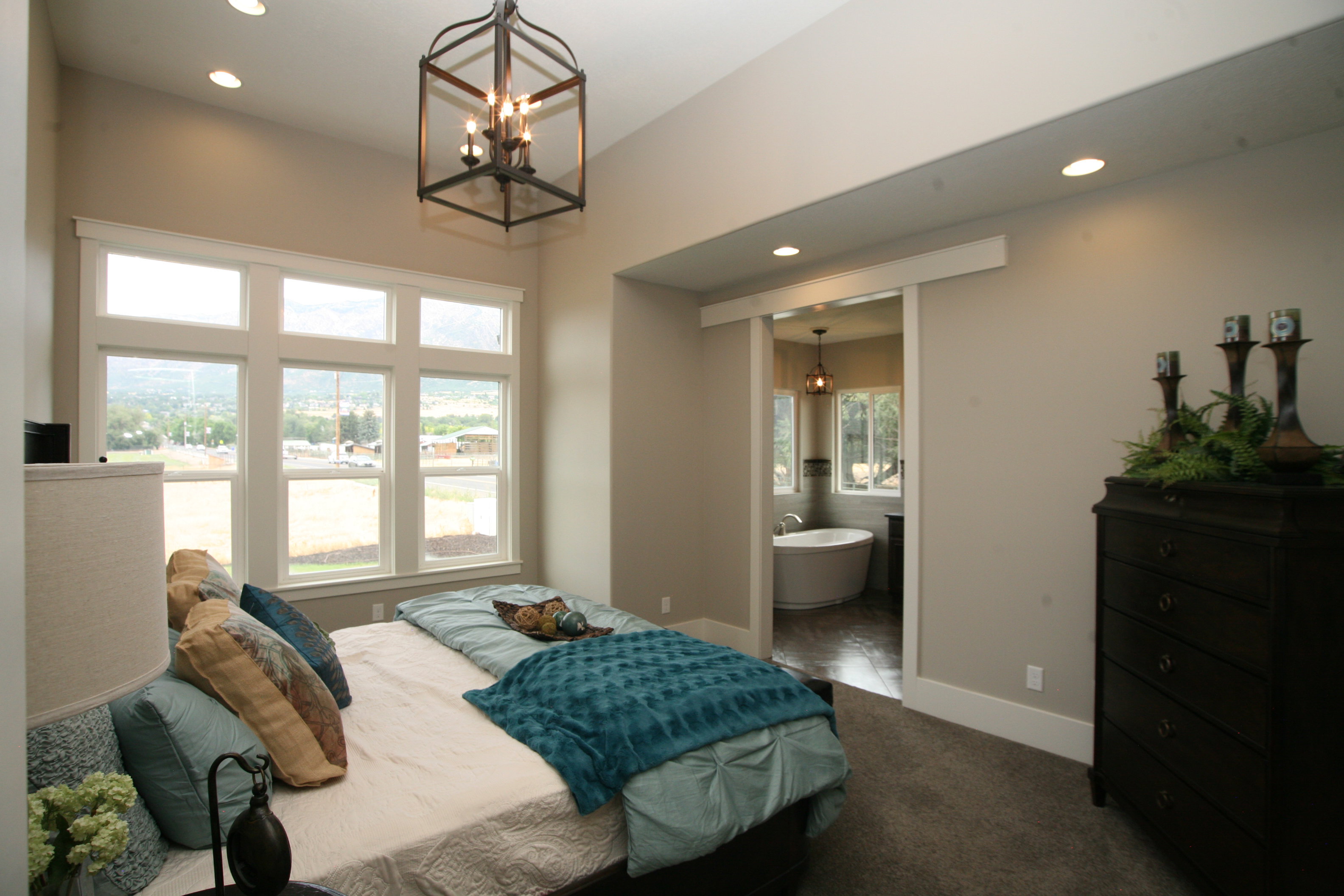 Spacious bedroom featuring a large window array, recessed lighting, and an overhead caged chandelier