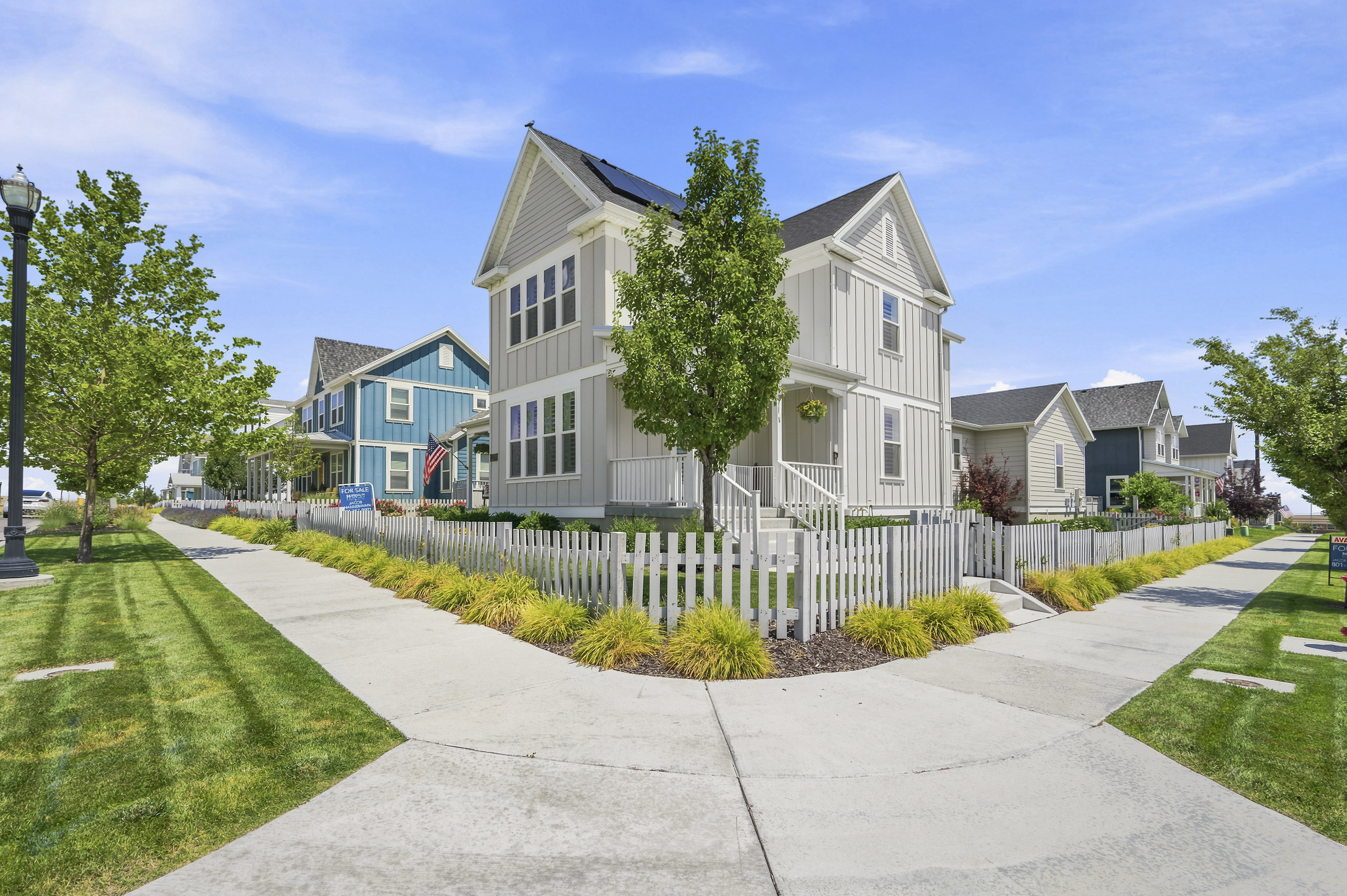 Two-story residence featuring light gray vertical siding, a front porch with white railings, and a white picket fence