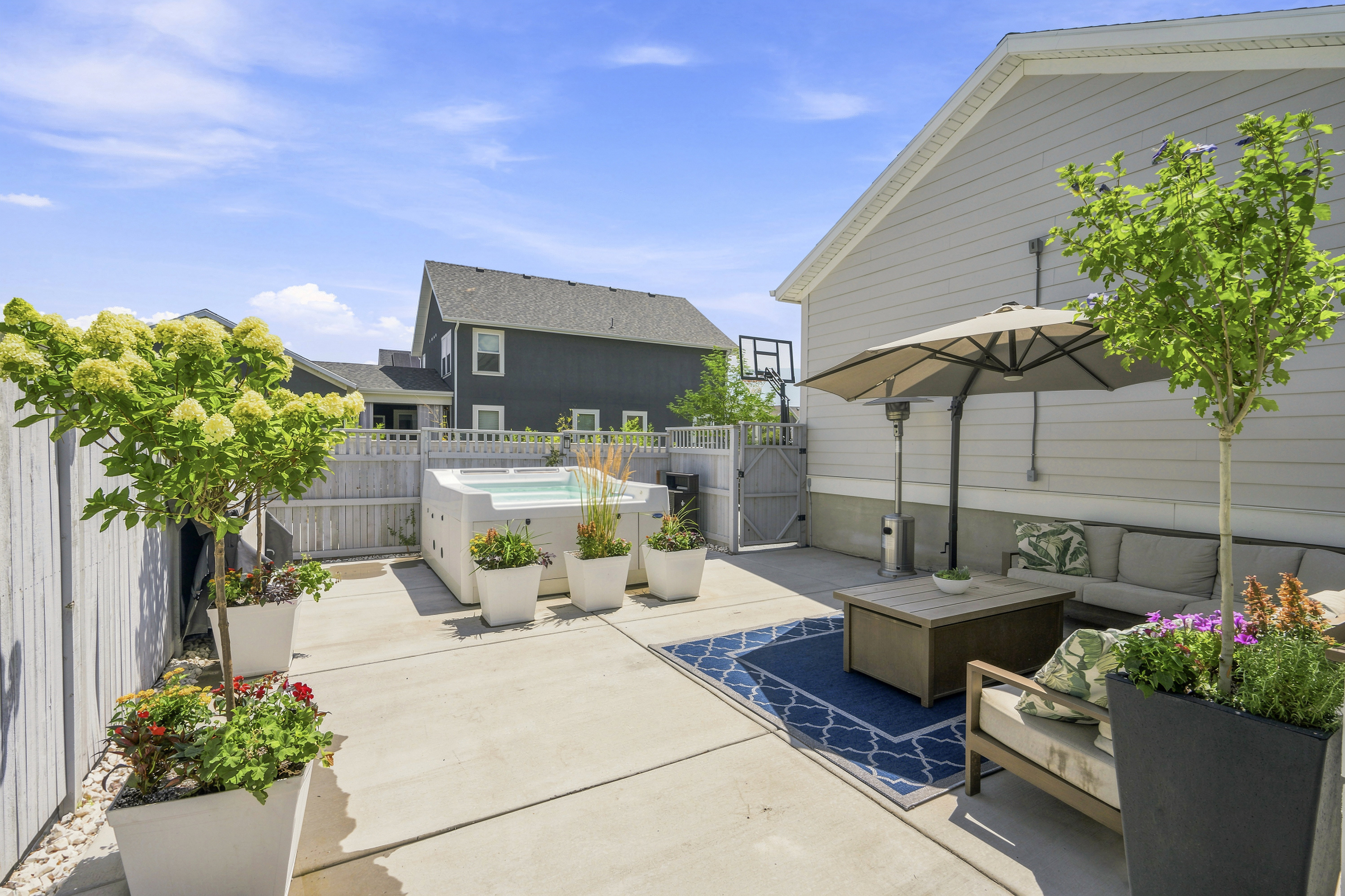 Paved patio featuring a built-in hot tub, privacy fencing, side yard gate, and mature potted landscaping