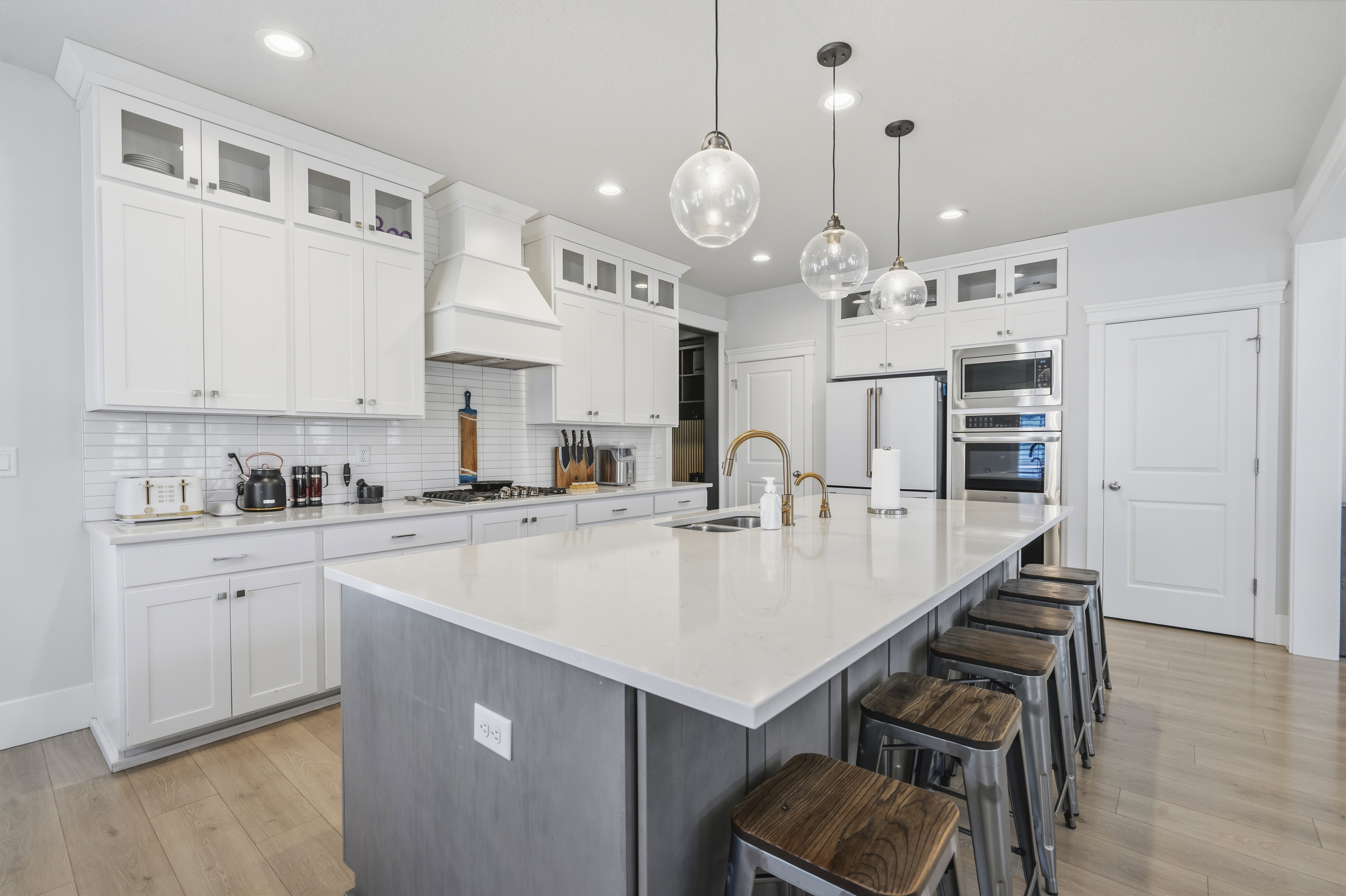 Spacious kitchen featuring an expansive central island with counter seating, white shaker cabinetry, stainless steel appliances, a subway tile backsplash, and light wood-finish flooring