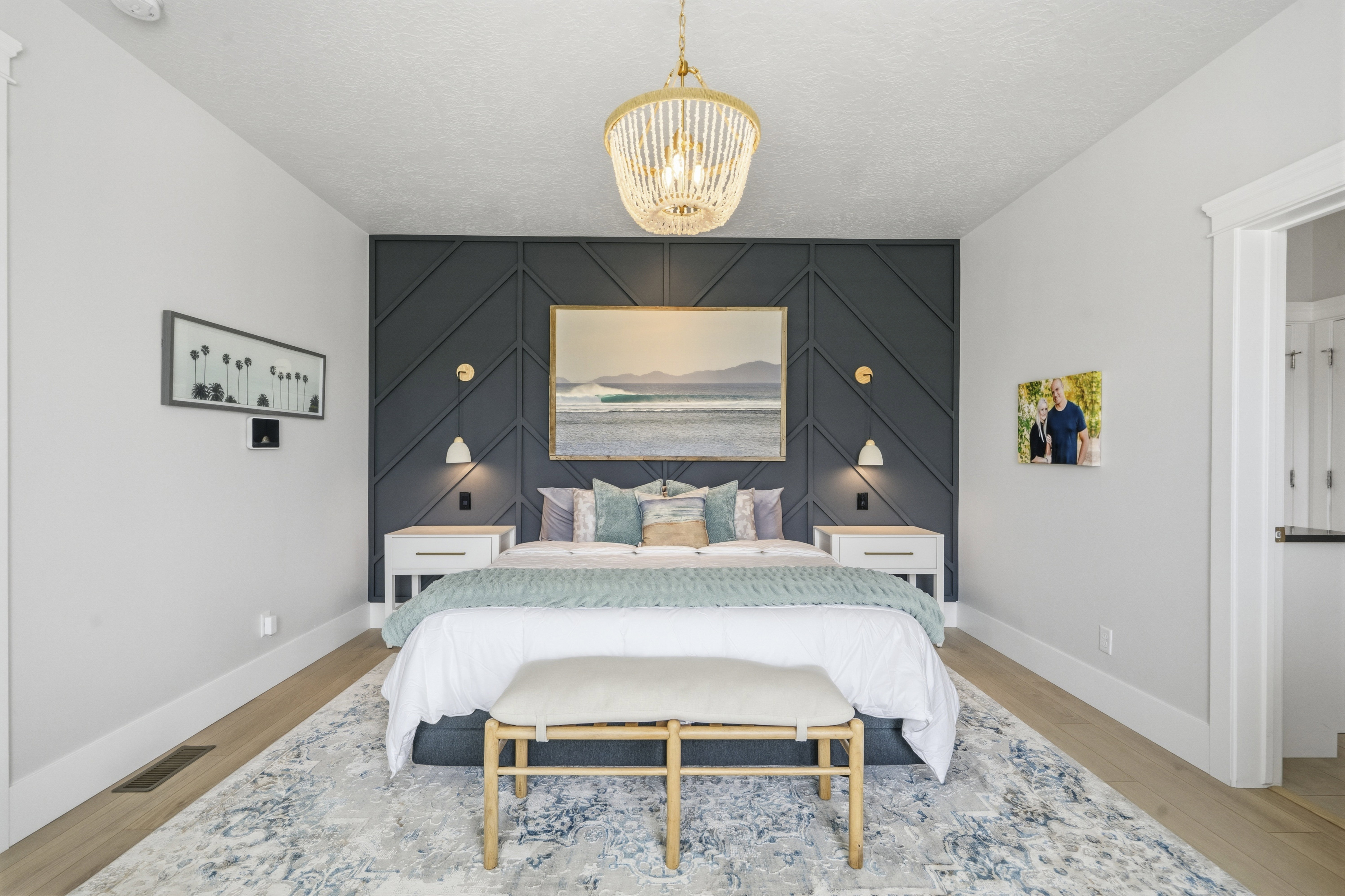 Bedroom featuring a decorative accent wall with geometric paneling, light wood-finish flooring, and a detailed overhead chandelier