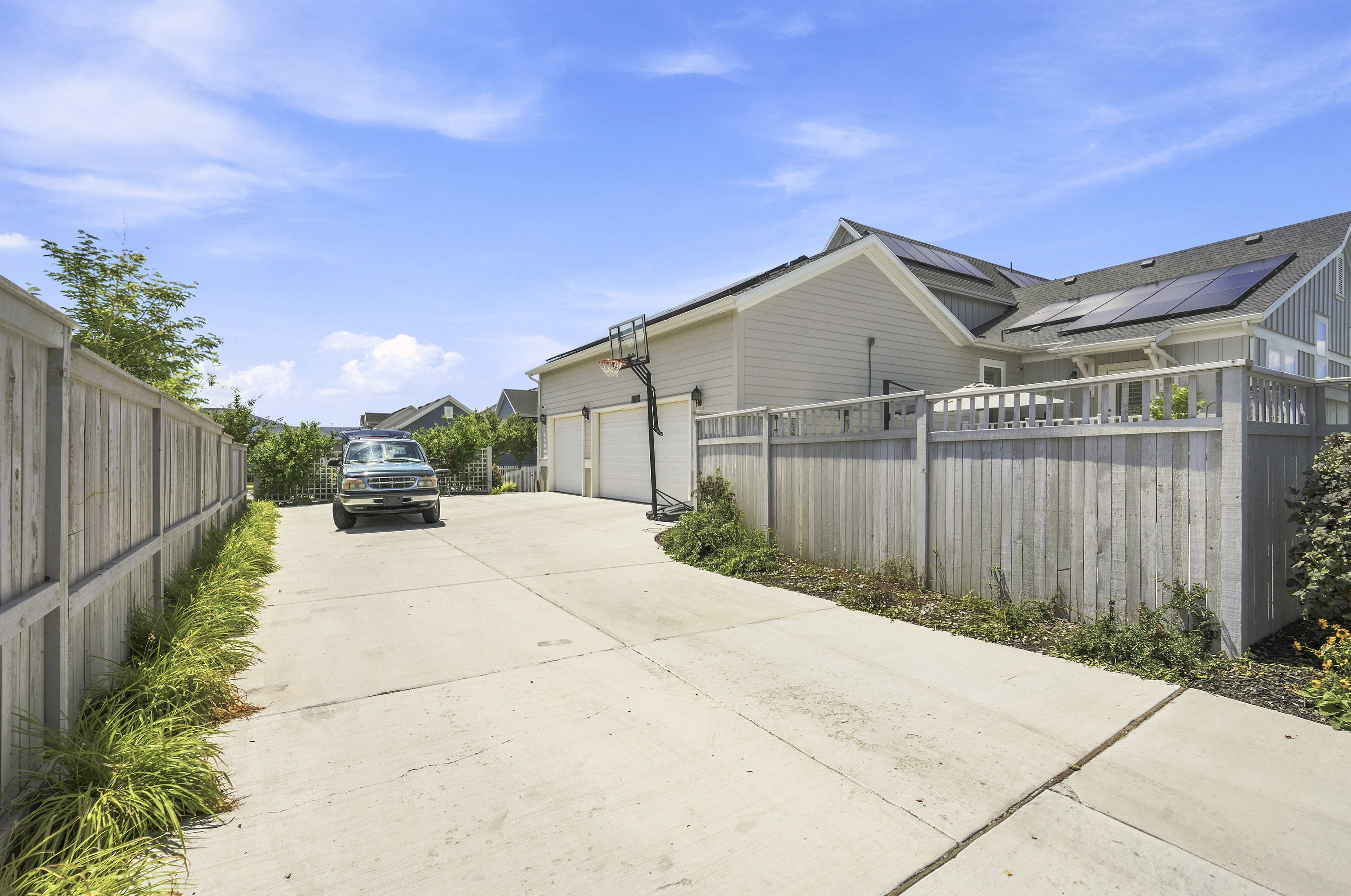 Extensive concrete driveway with perimeter fencing and mature landscaping, leading to a two-car garage with white paneled doors
