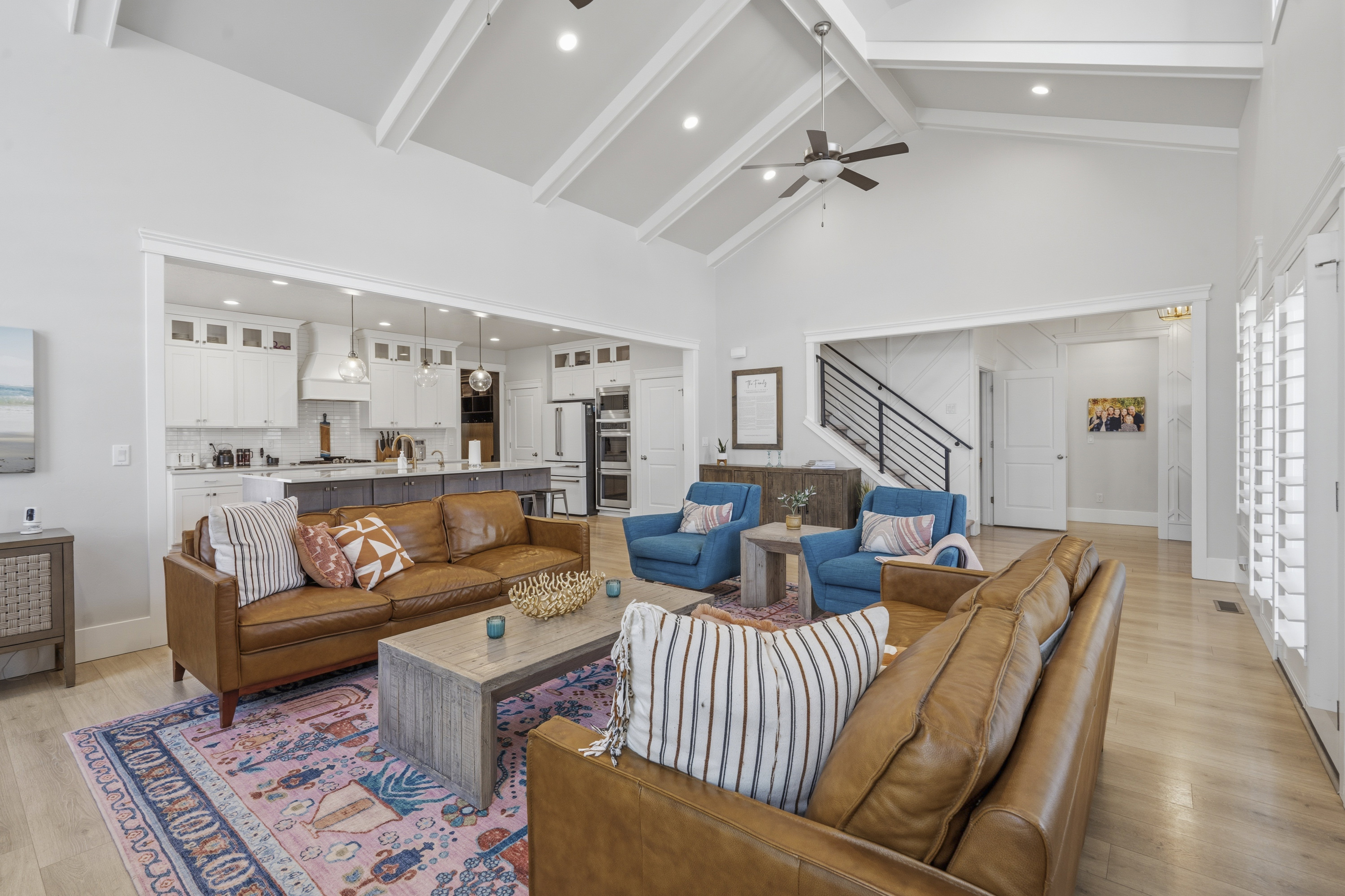 Open-concept living space featuring vaulted ceilings with exposed beams, light wood-finish flooring, and white plantation shutters