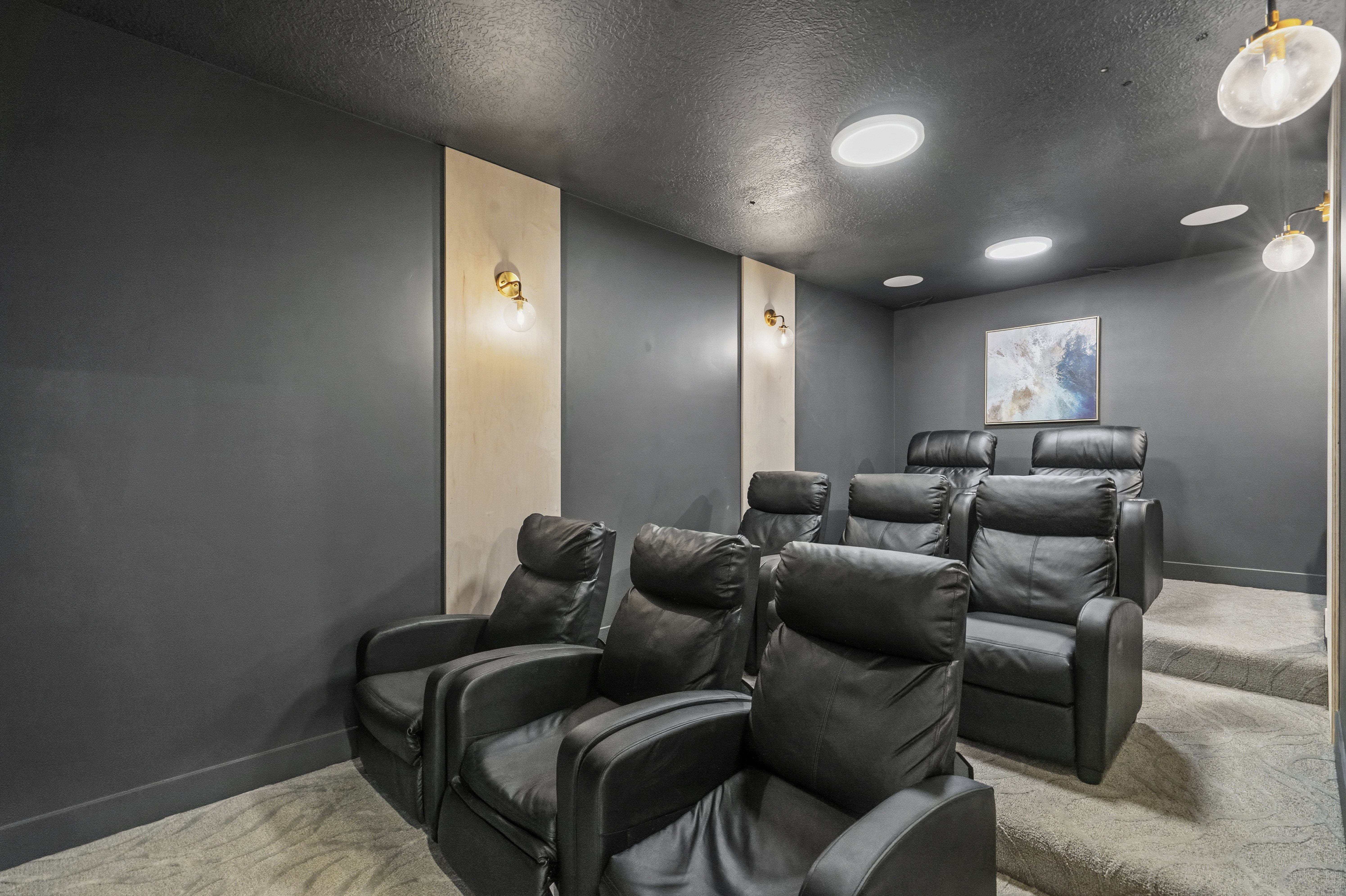 Dedicated home theater featuring tiered seating, recessed ceiling lighting, wall-mounted sconces, and plush carpet flooring