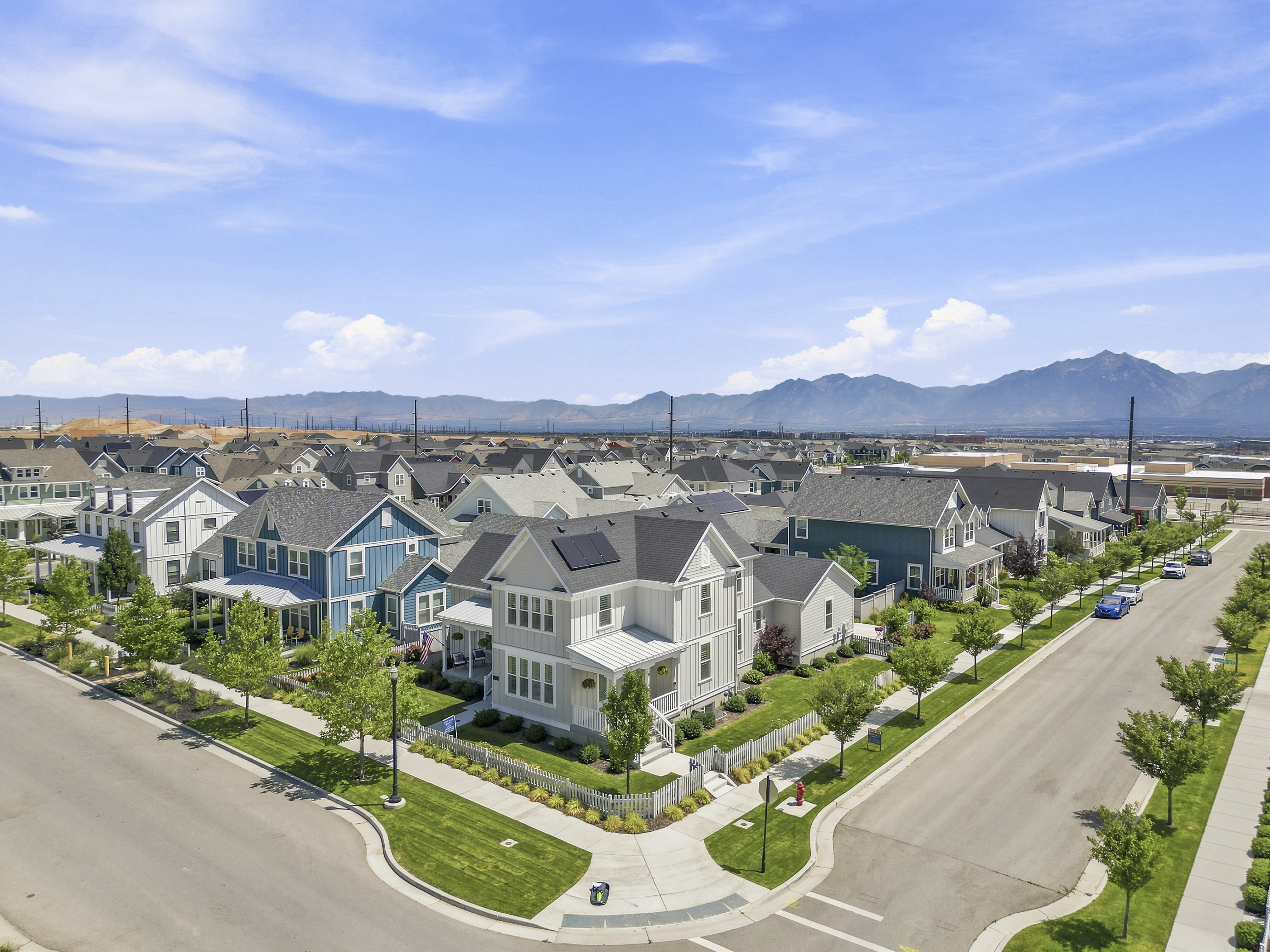 Modern residential neighborhood featuring a mix of architectural styles, tree-lined streets, sidewalks, and mountain scenery in the distance