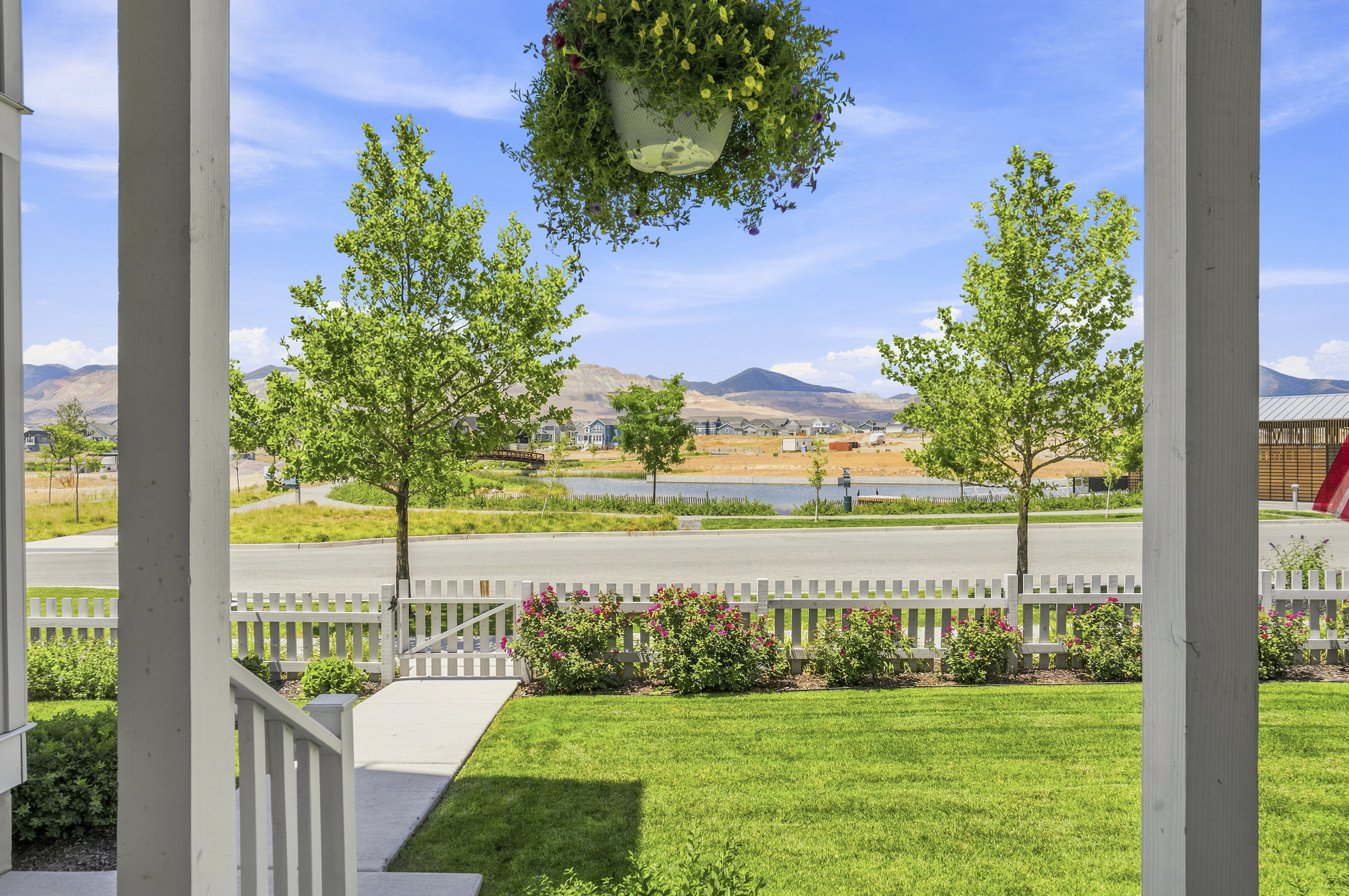 Front porch framing a manicured lawn with a white picket fence, a concrete walkway, and established landscaping