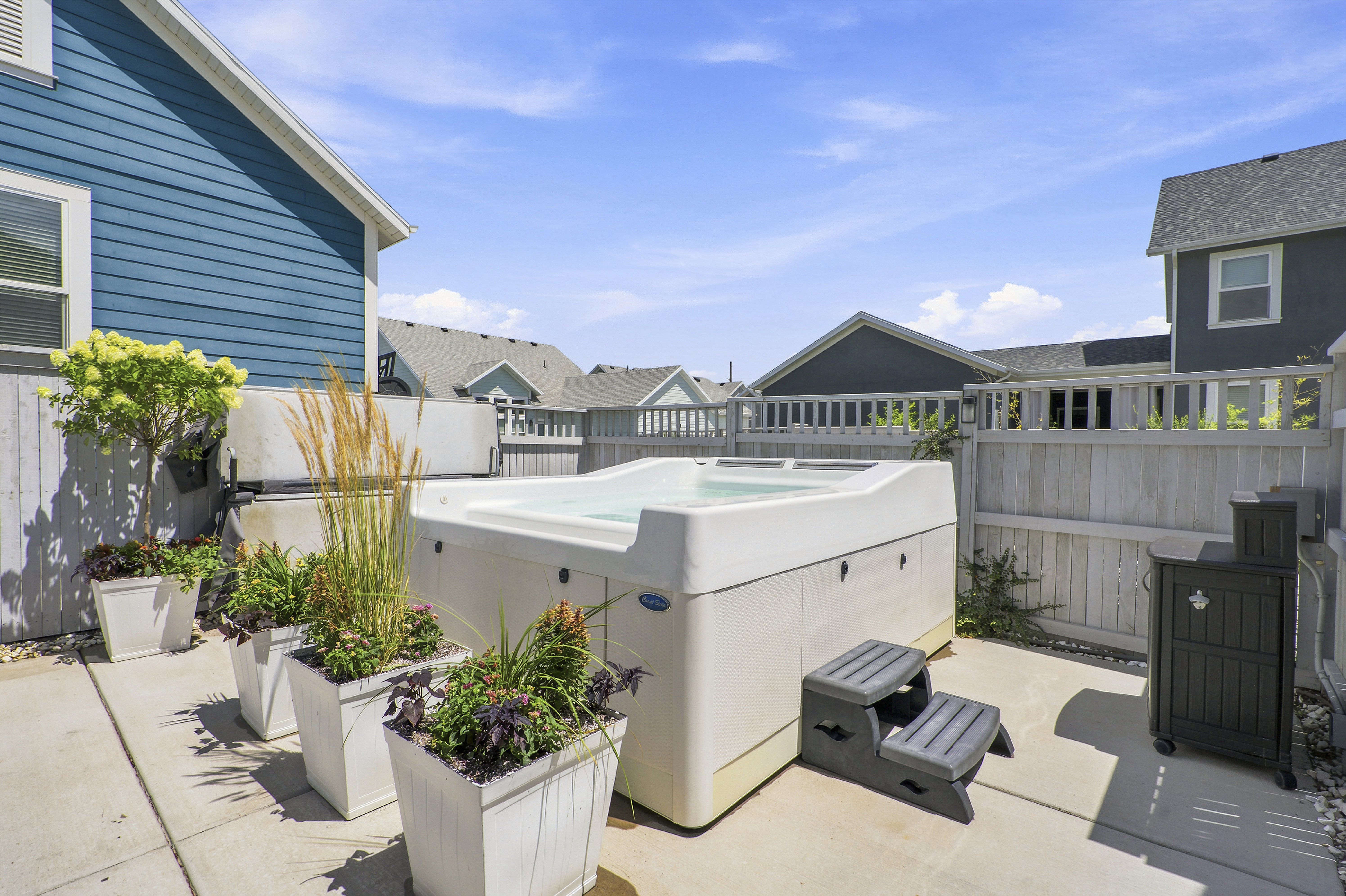 Outdoor patio featuring a hot tub with steps, multiple potted plants, and concrete paving