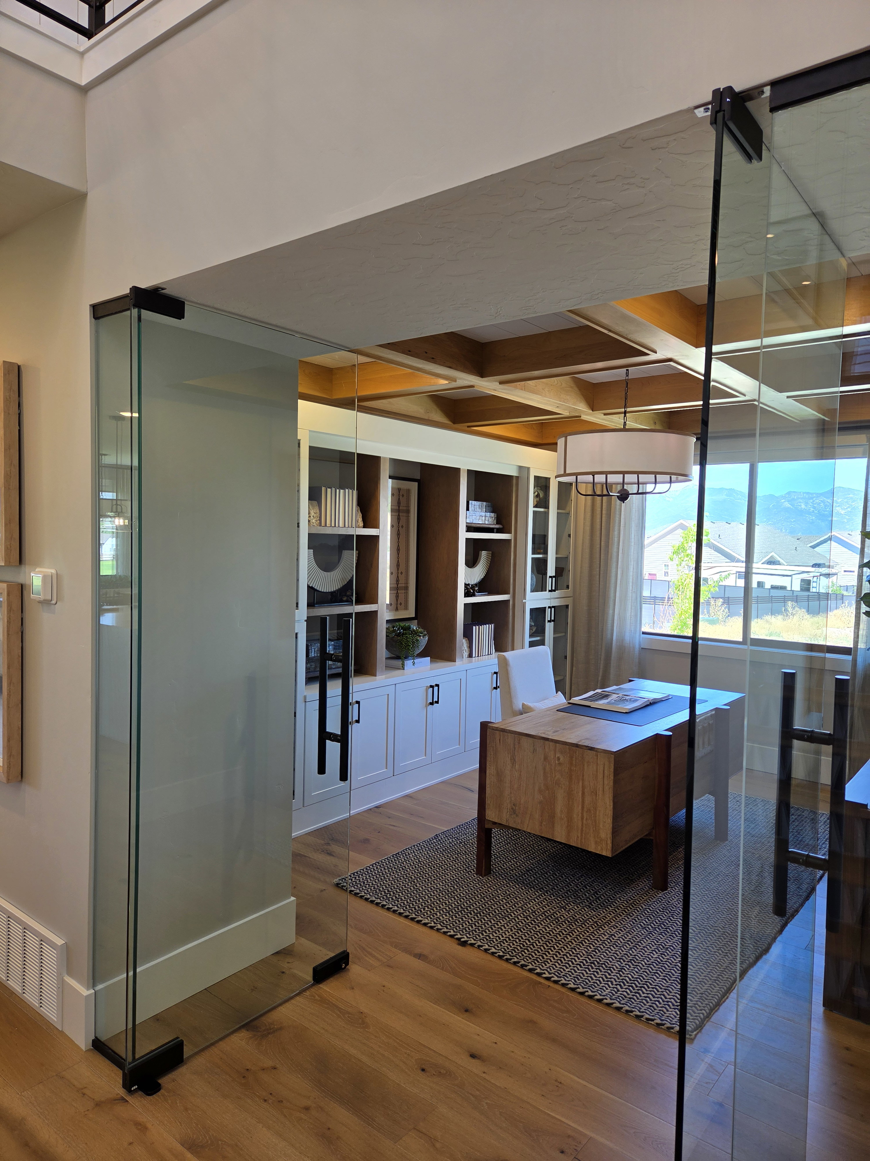 Glass-enclosed room featuring a coffered ceiling with wood accents, wood-finish flooring, built-in cabinetry, and a contemporary chandelier