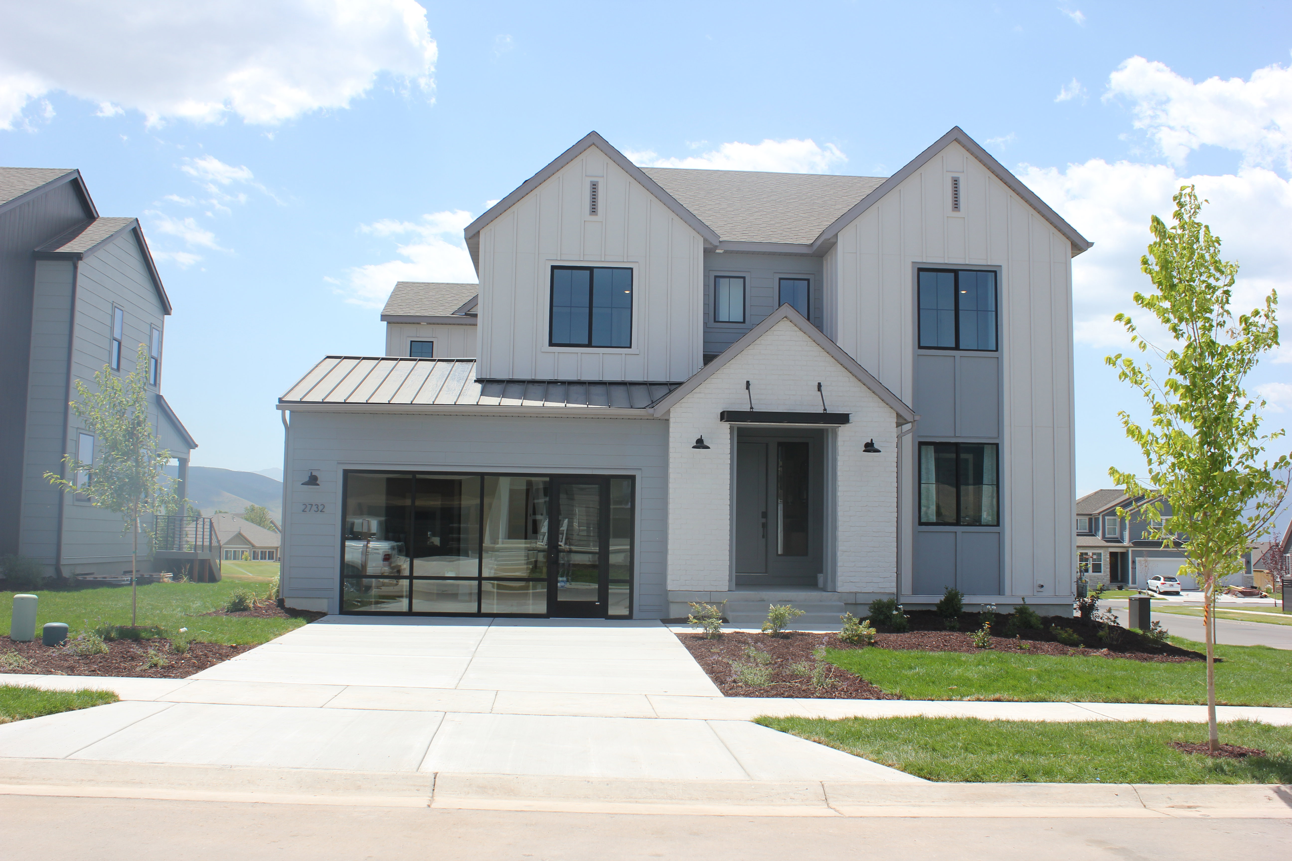 Modern farmhouse exterior featuring board and batten siding, brick accents, and a metal roof over the garage