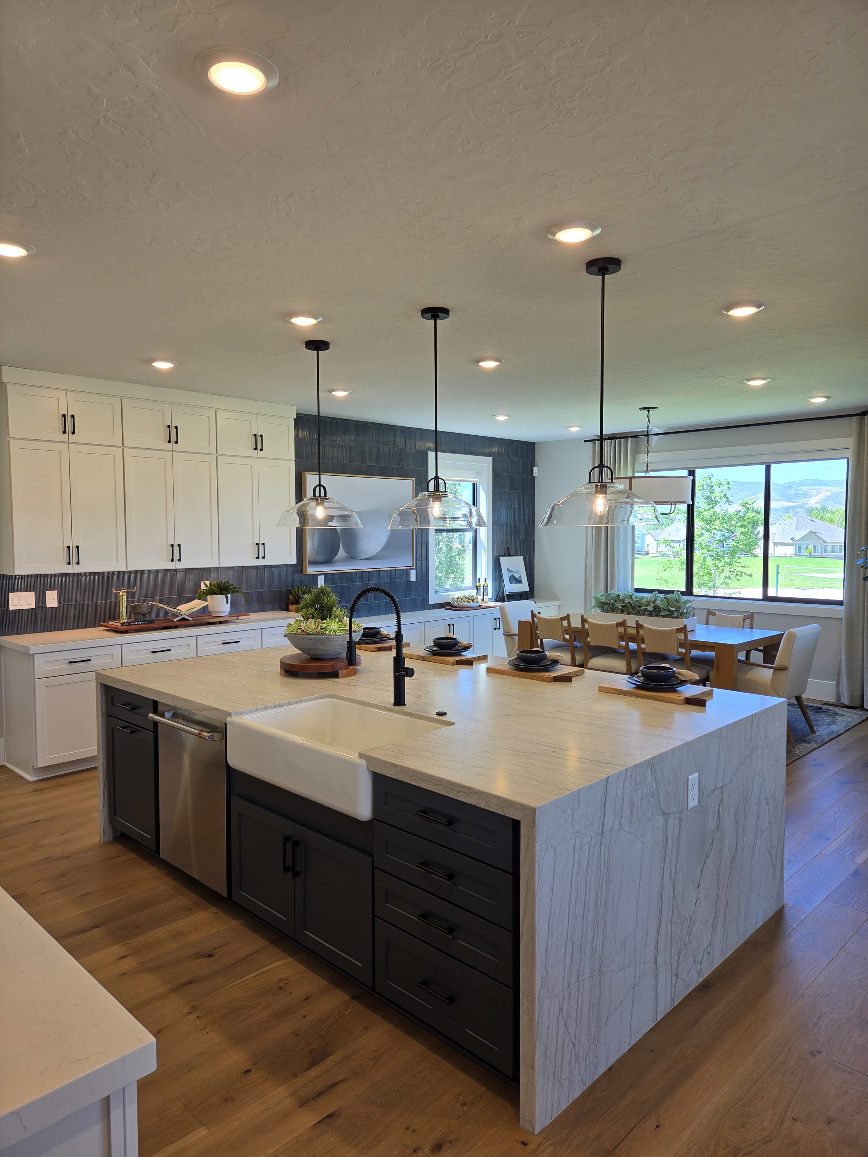 Expansive kitchen island featuring a farmhouse sink, integrated dishwasher, and a waterfall-edge countertop