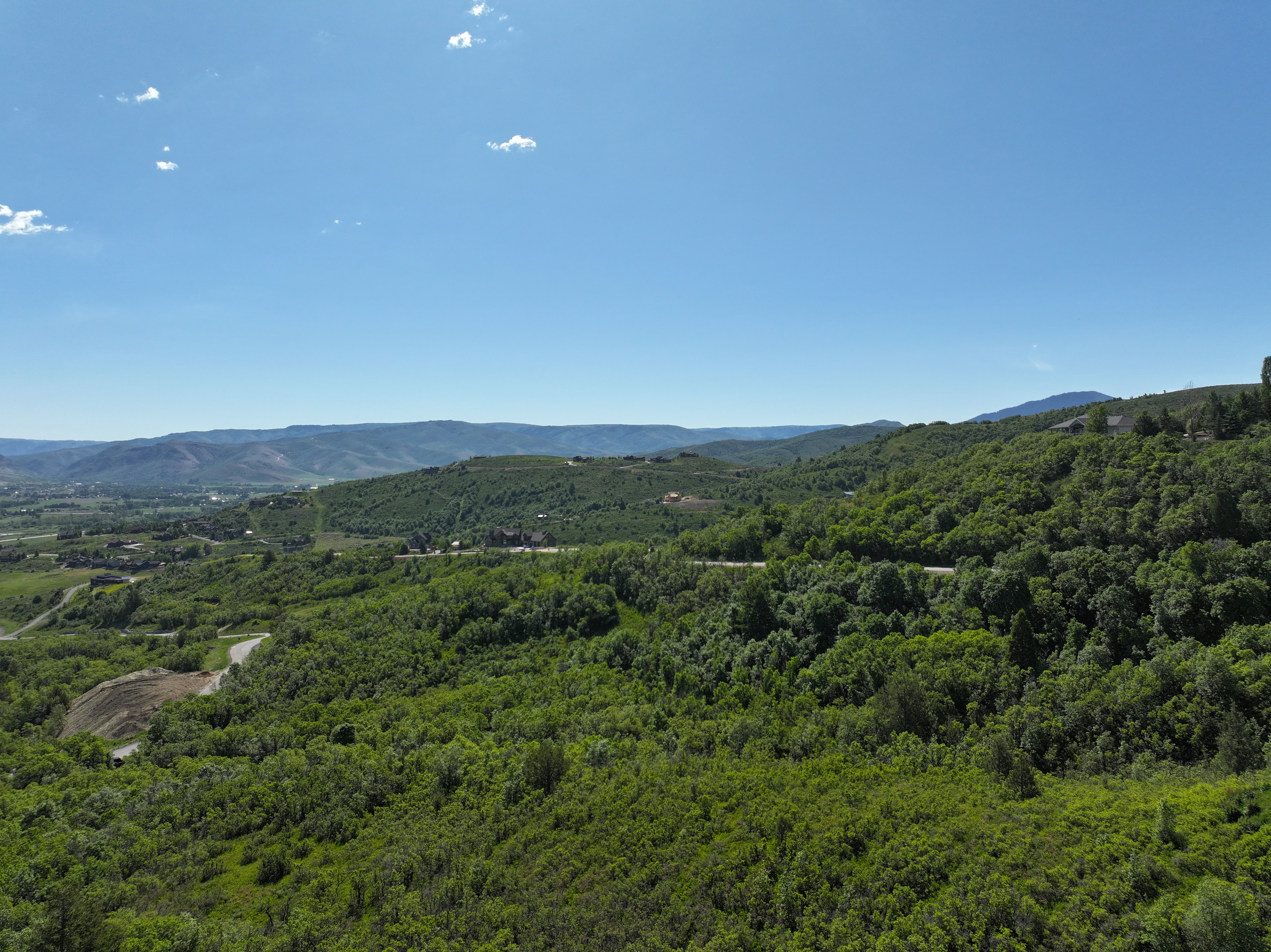 Expansive mountain landscape featuring abundant green foliage and distant mountain ranges under a clear sky