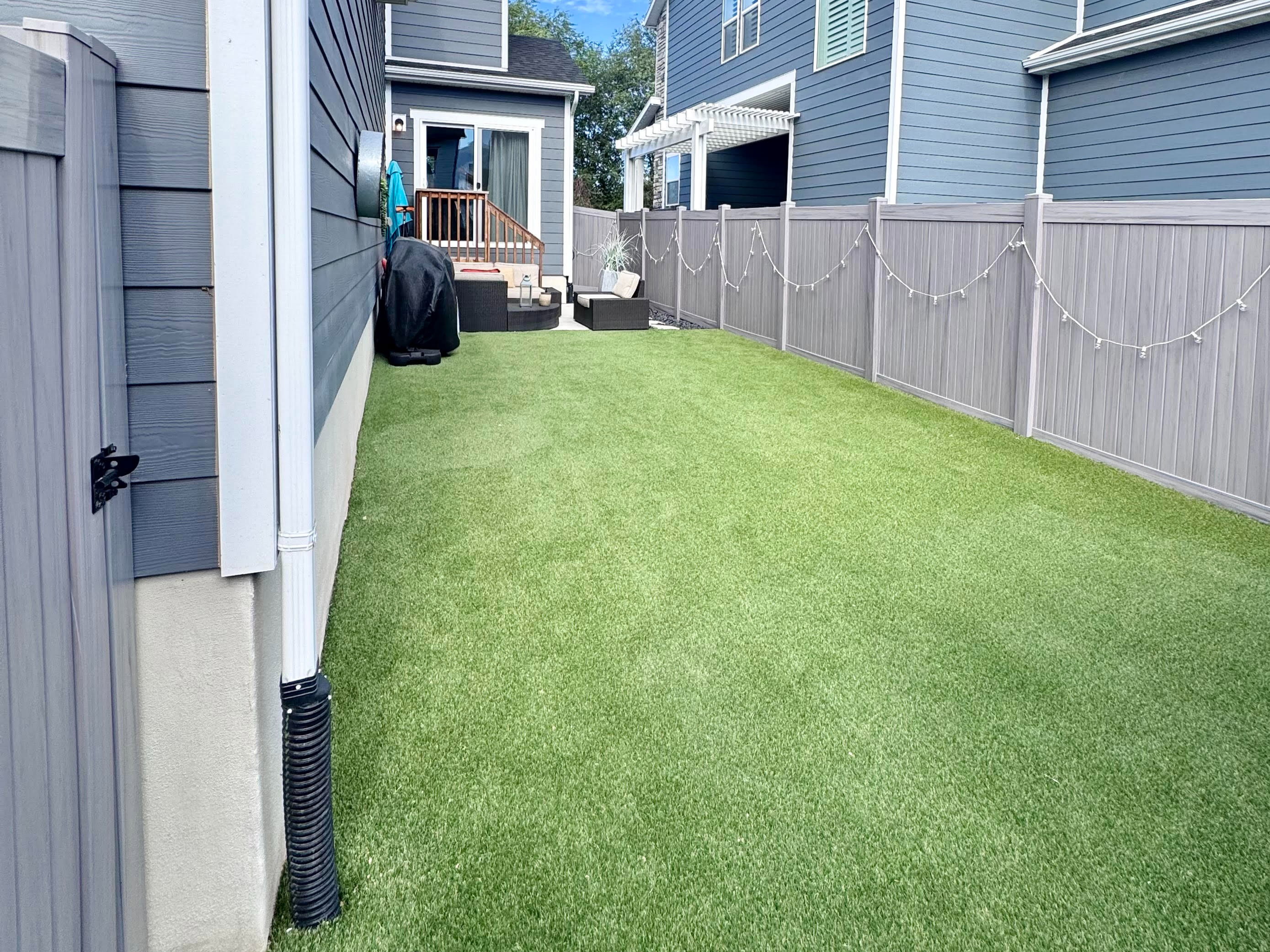 Fully fenced backyard featuring artificial turf, a wood deck with stairs, and a white pergola