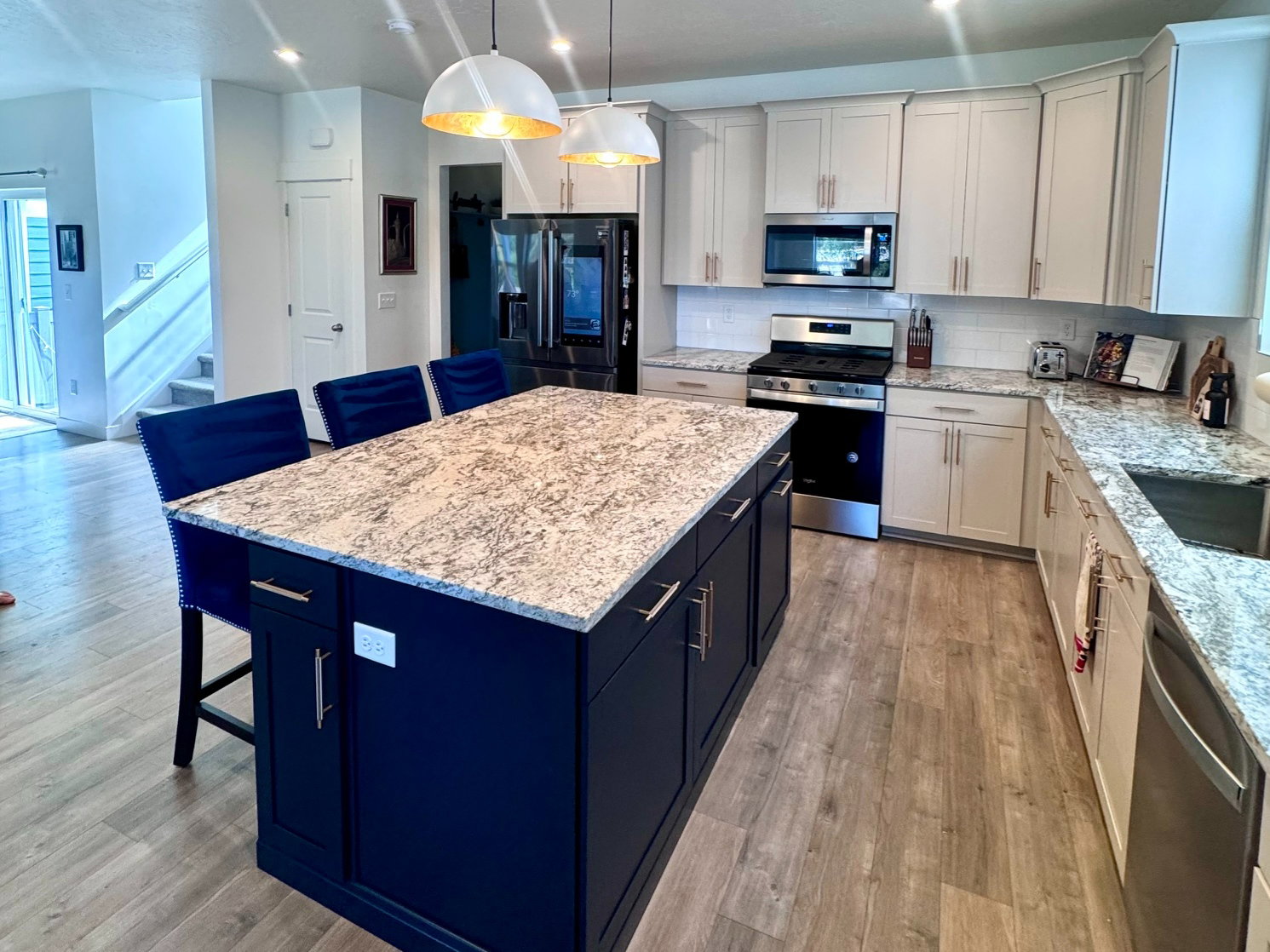 Spacious kitchen featuring a large central island with a light-colored countertop, white upper and lower cabinetry, stainless steel appliances, and wood-finish flooring