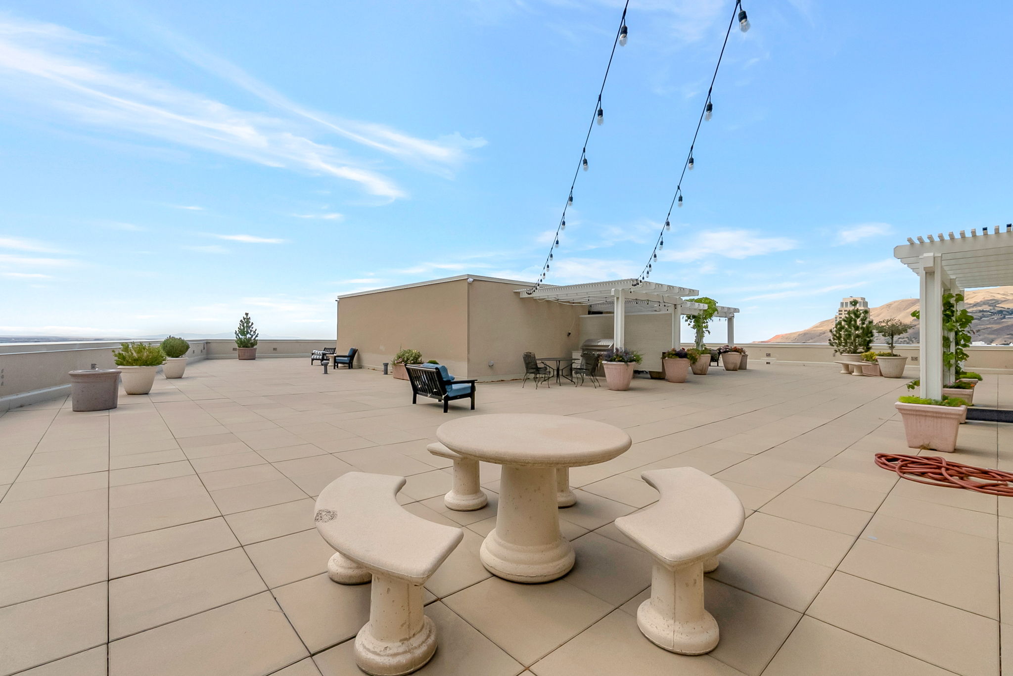Expansive rooftop patio featuring large format tile flooring, string lighting, and multiple pergolas providing shaded areas