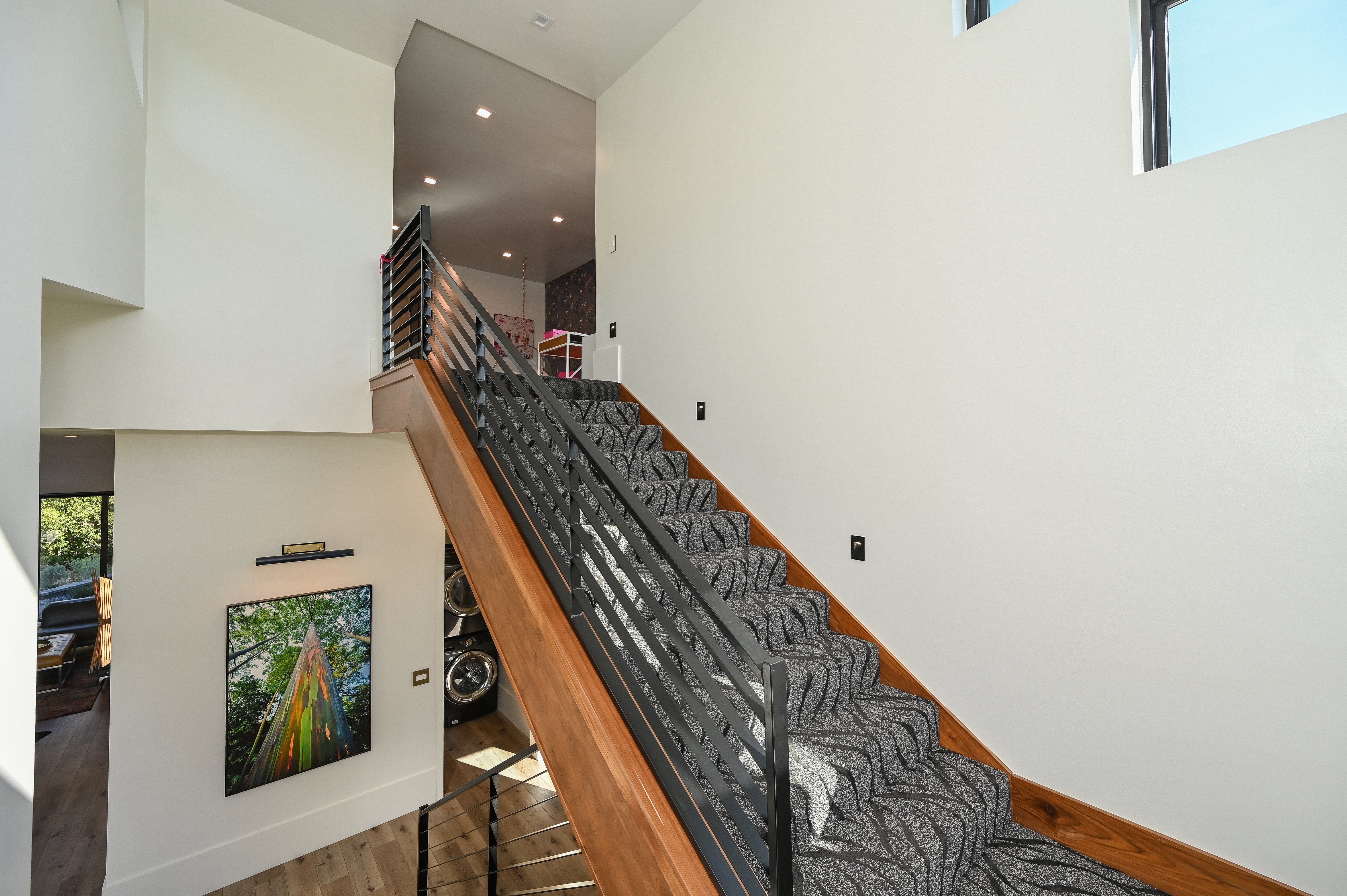 Modern staircase featuring wood-finish treads, a patterned carpet runner, and metal railings