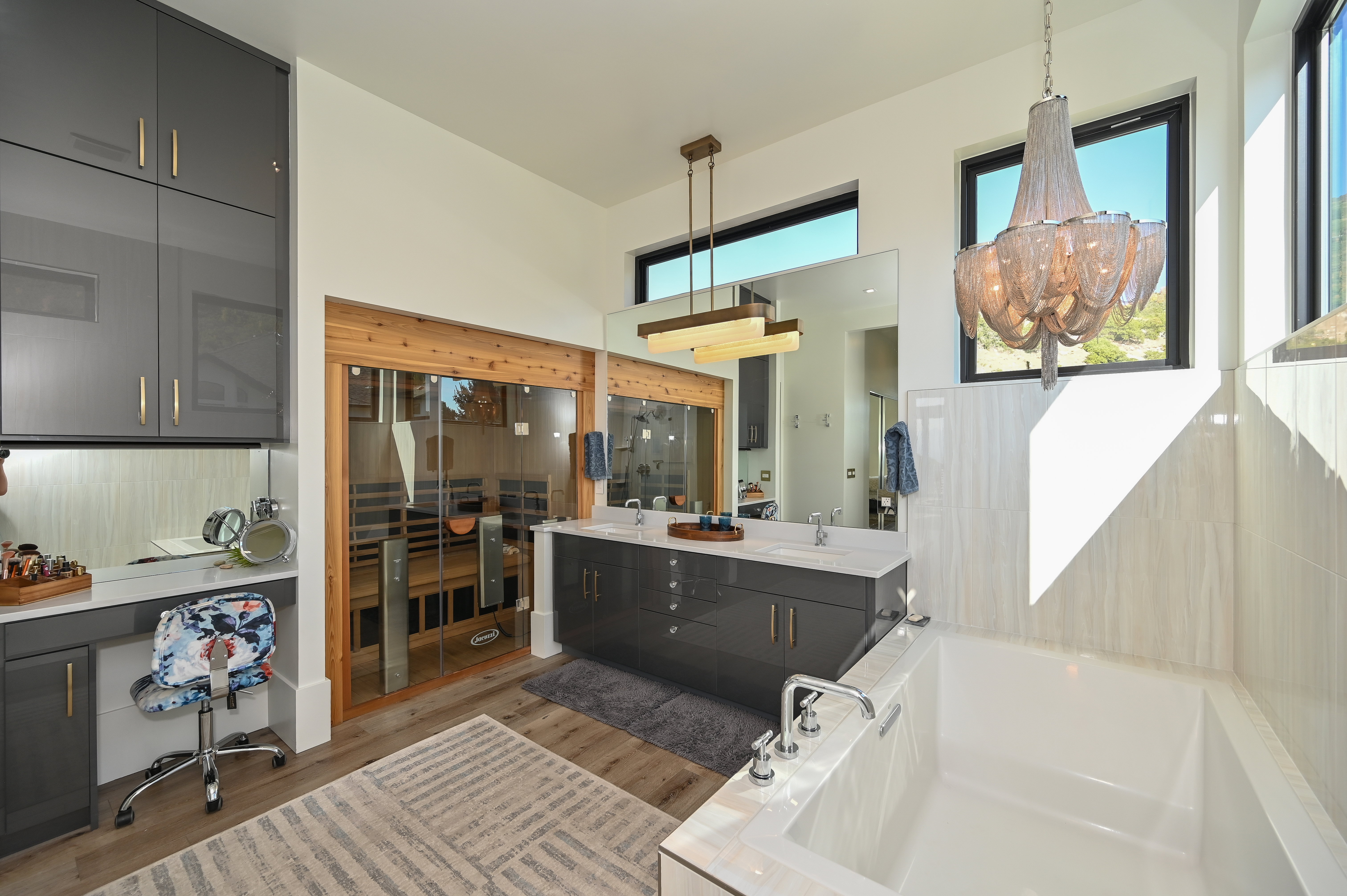 Bathroom featuring a built-in sauna with glass doors, a freestanding soaking tub, dual vanity with quartz countertop, wood-finish flooring, and a makeup vanity with storage