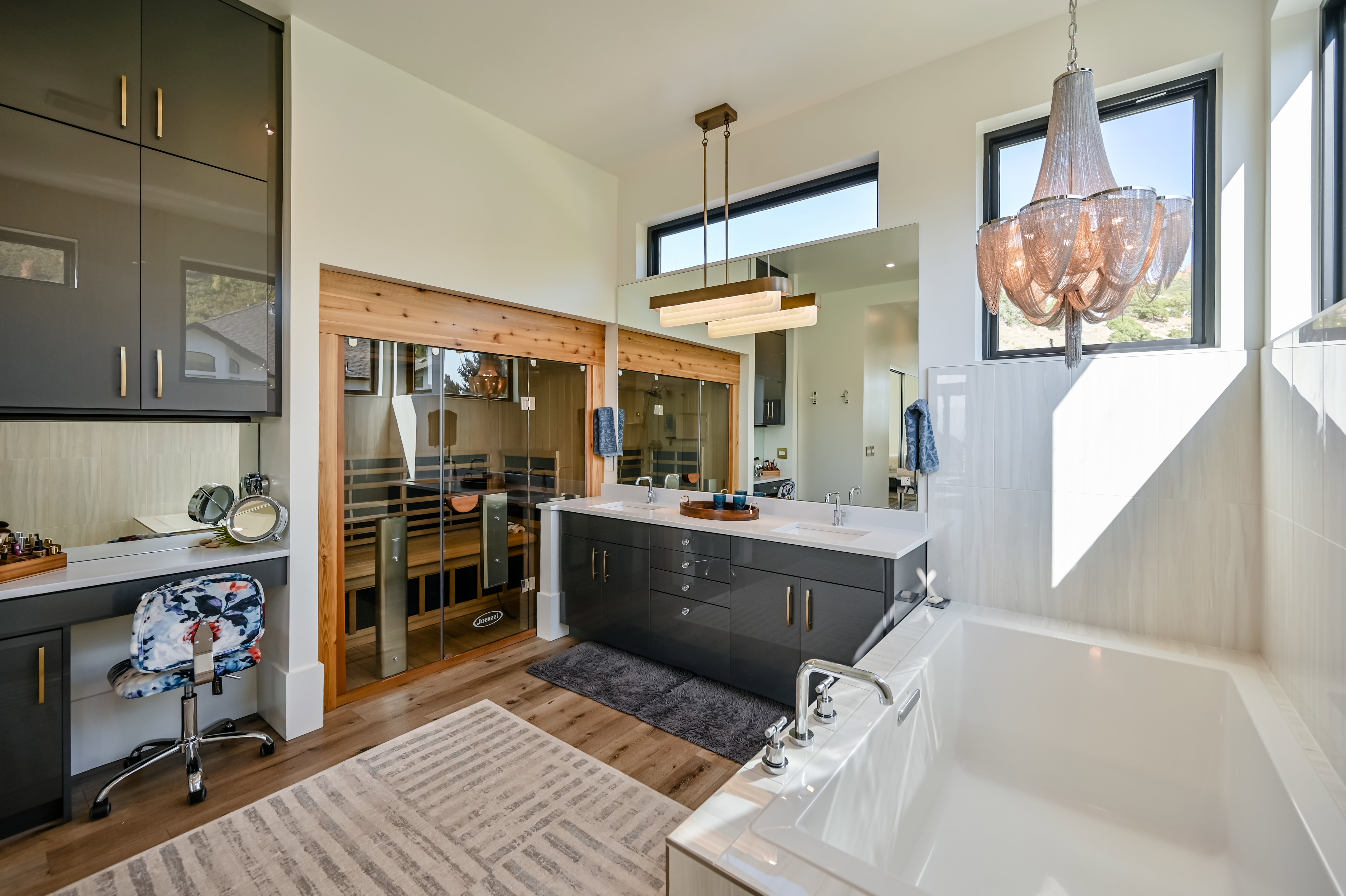 Contemporary bathroom featuring a built-in sauna with glass doors, a dual vanity with undermount sinks and quartz countertops, a large soaking tub with deck-mounted fixtures, and a vanity area with built-in cabinetry and a mirror