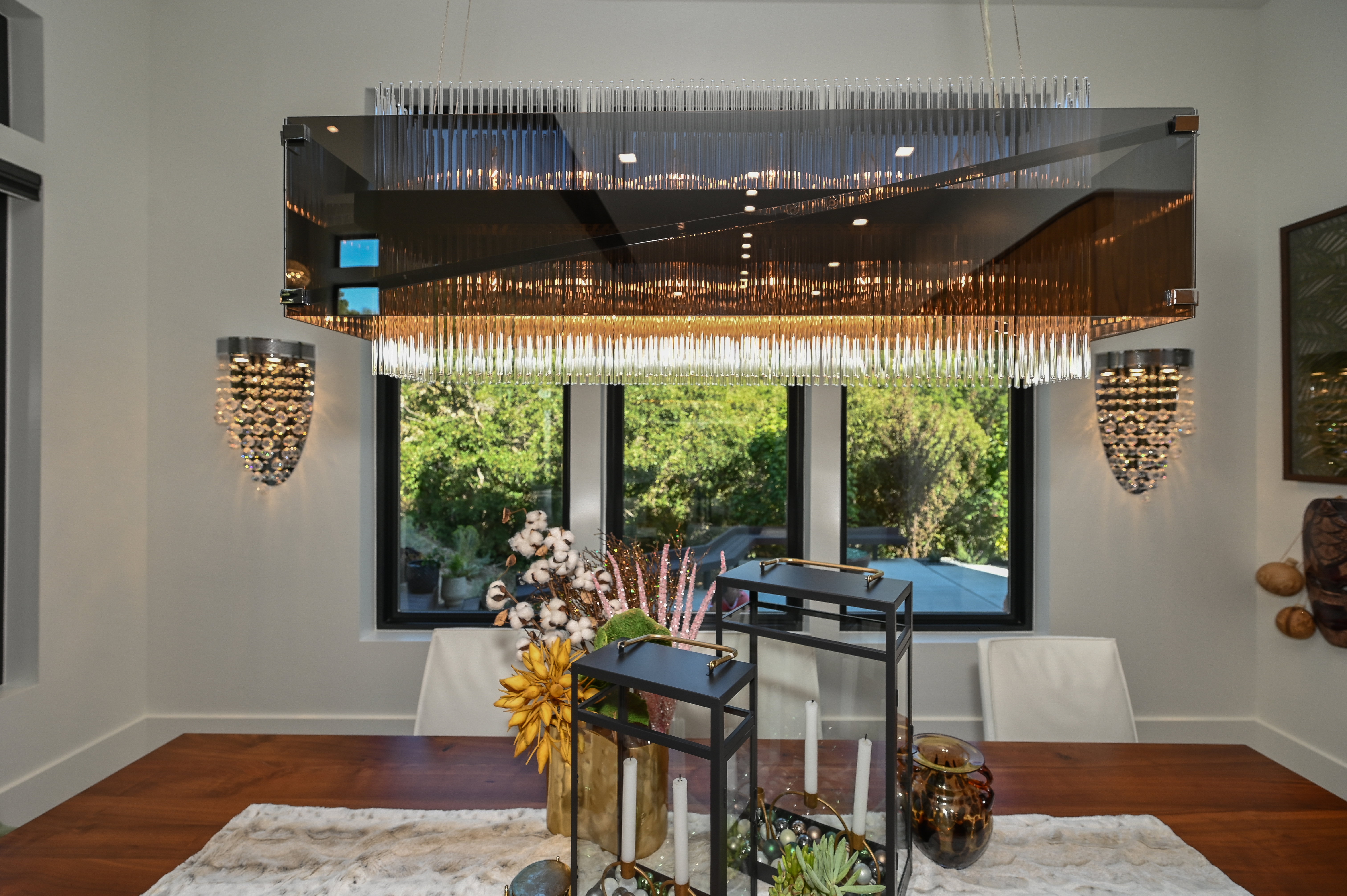 Contemporary dining area featuring a distinctive rectangular chandelier with glass rods, wood-finish flooring, and crisp white walls