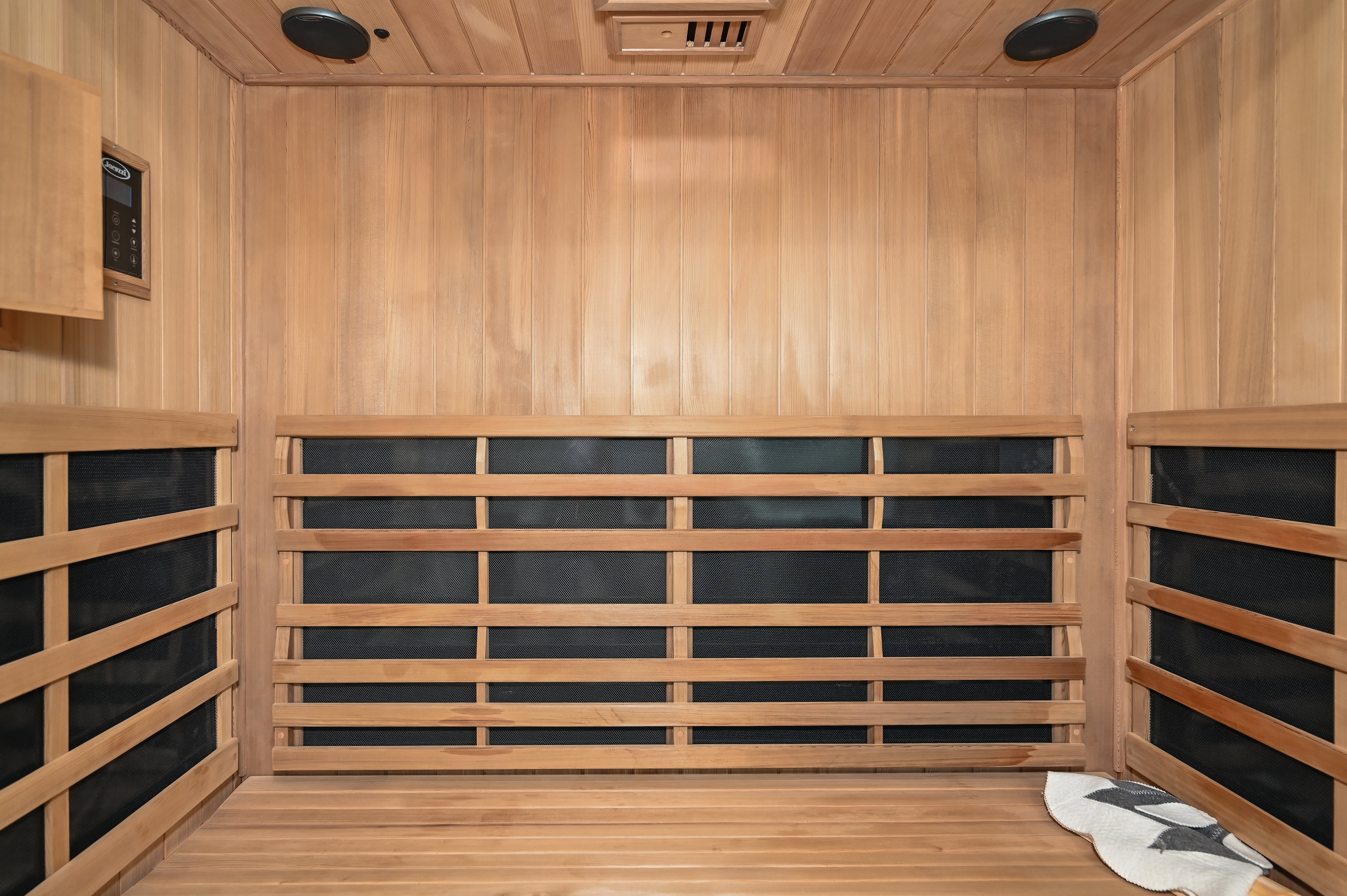 Infrared sauna featuring slat-wood walls and seating, built-in ceiling speakers, and digital controls
