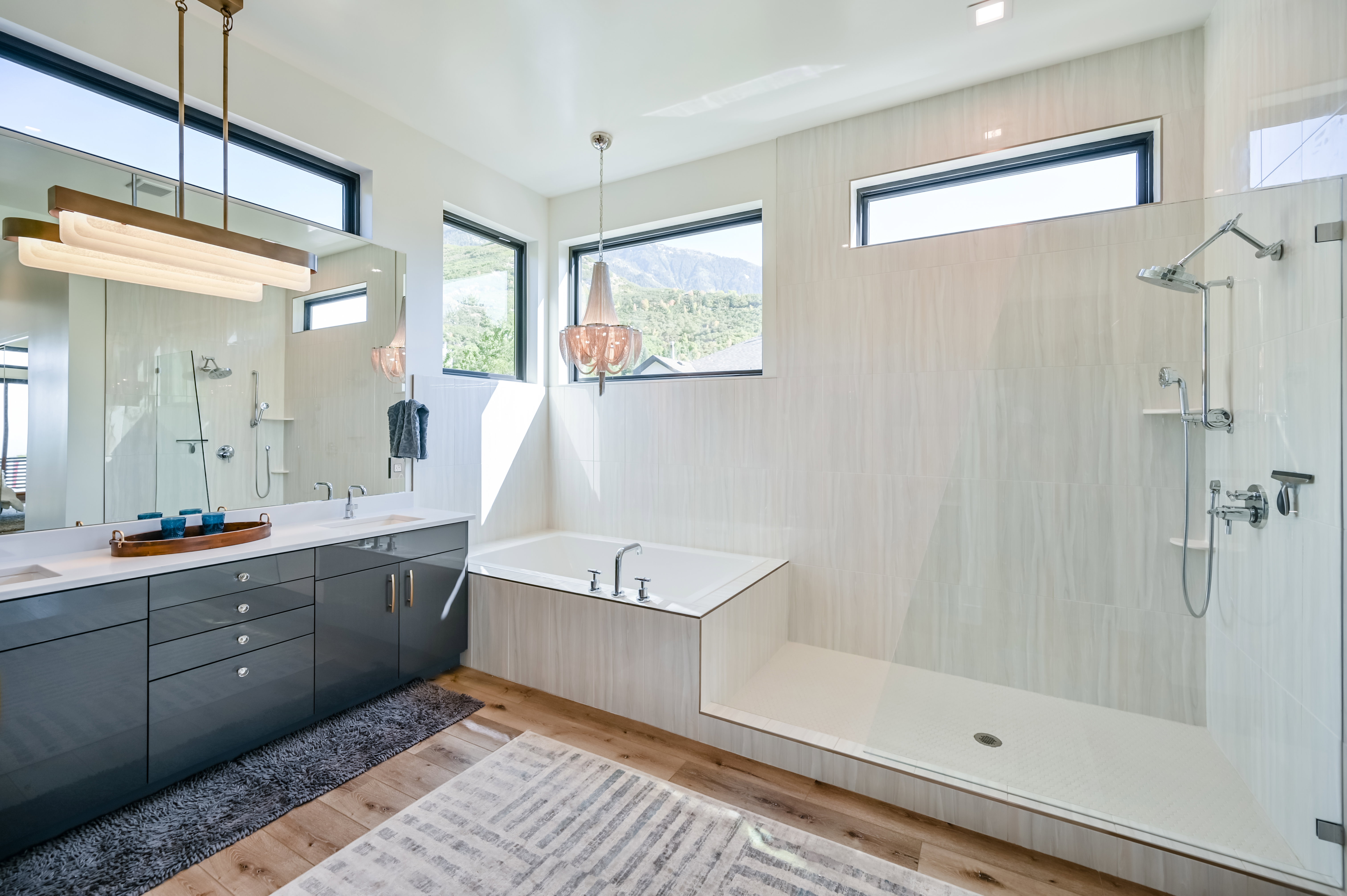 Bathroom featuring a dual vanity with a quartz countertop, a built-in soaking tub, a walk-in shower with glass enclosure, wood-finish flooring, and multiple transom windows