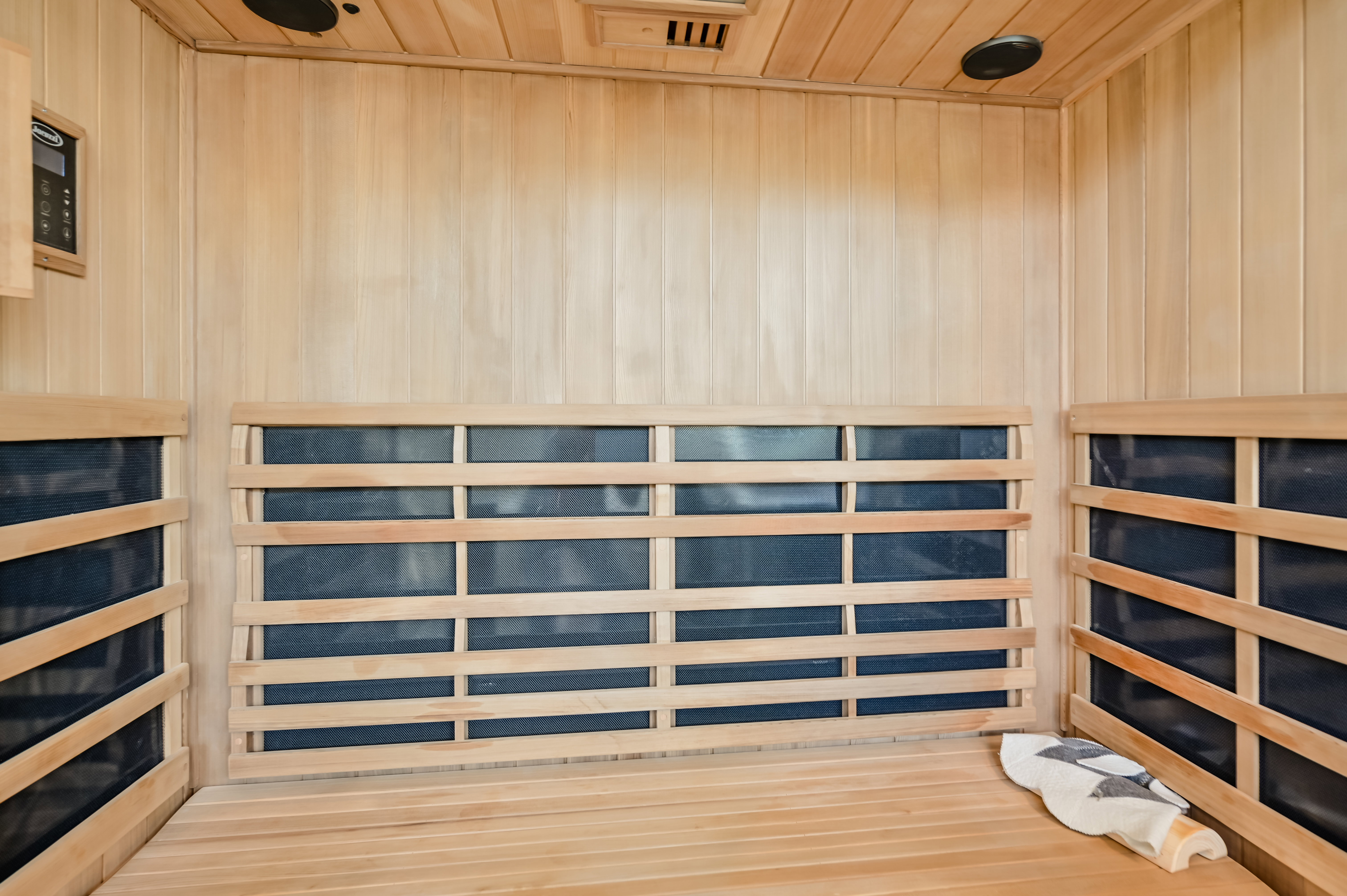 Dedicated sauna room featuring light-toned wood paneling, slatted wood benches, and integrated control panel