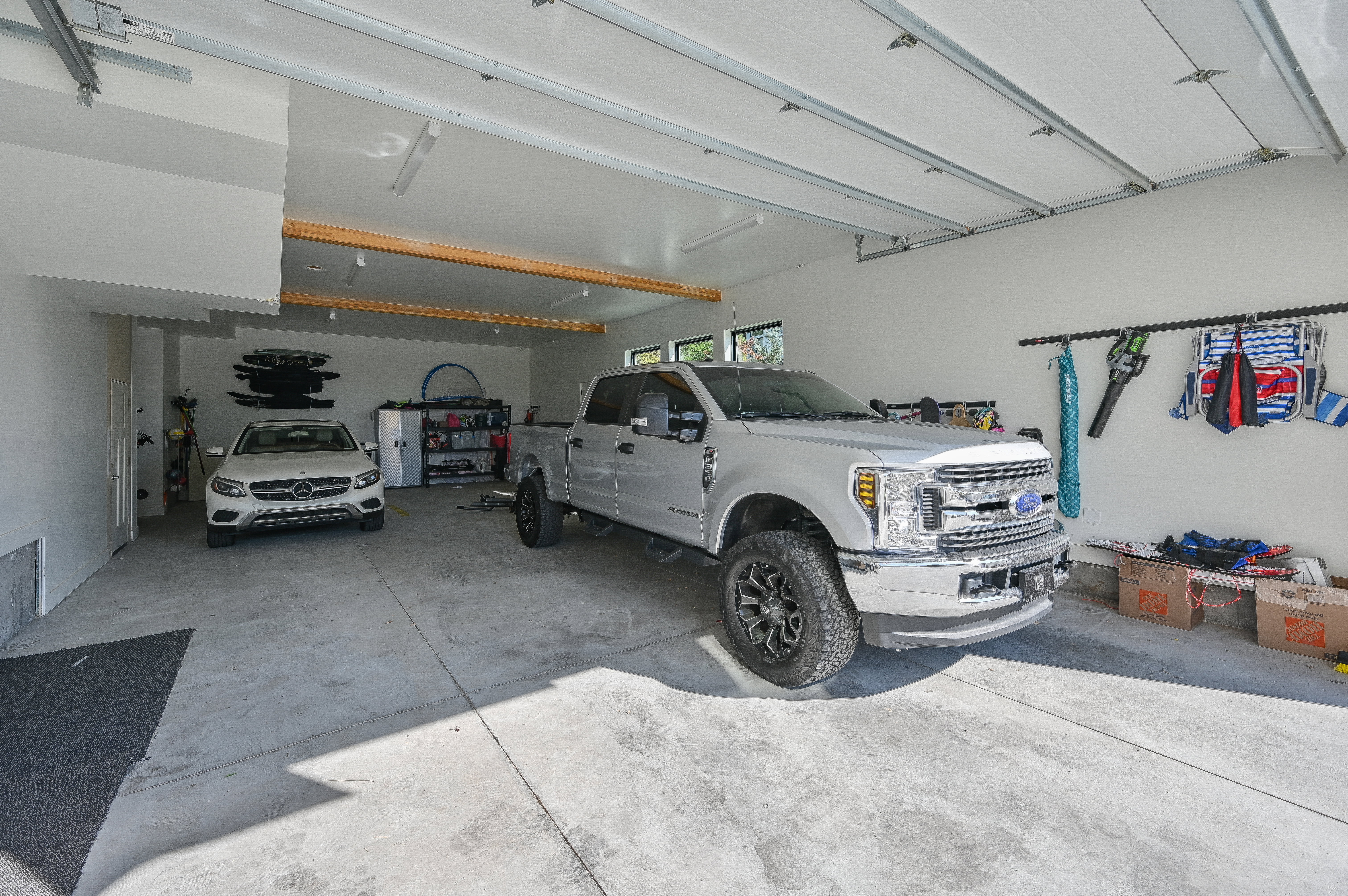 Spacious garage featuring a concrete floor, bright overhead lighting, exposed ceiling joists, and multiple storage options