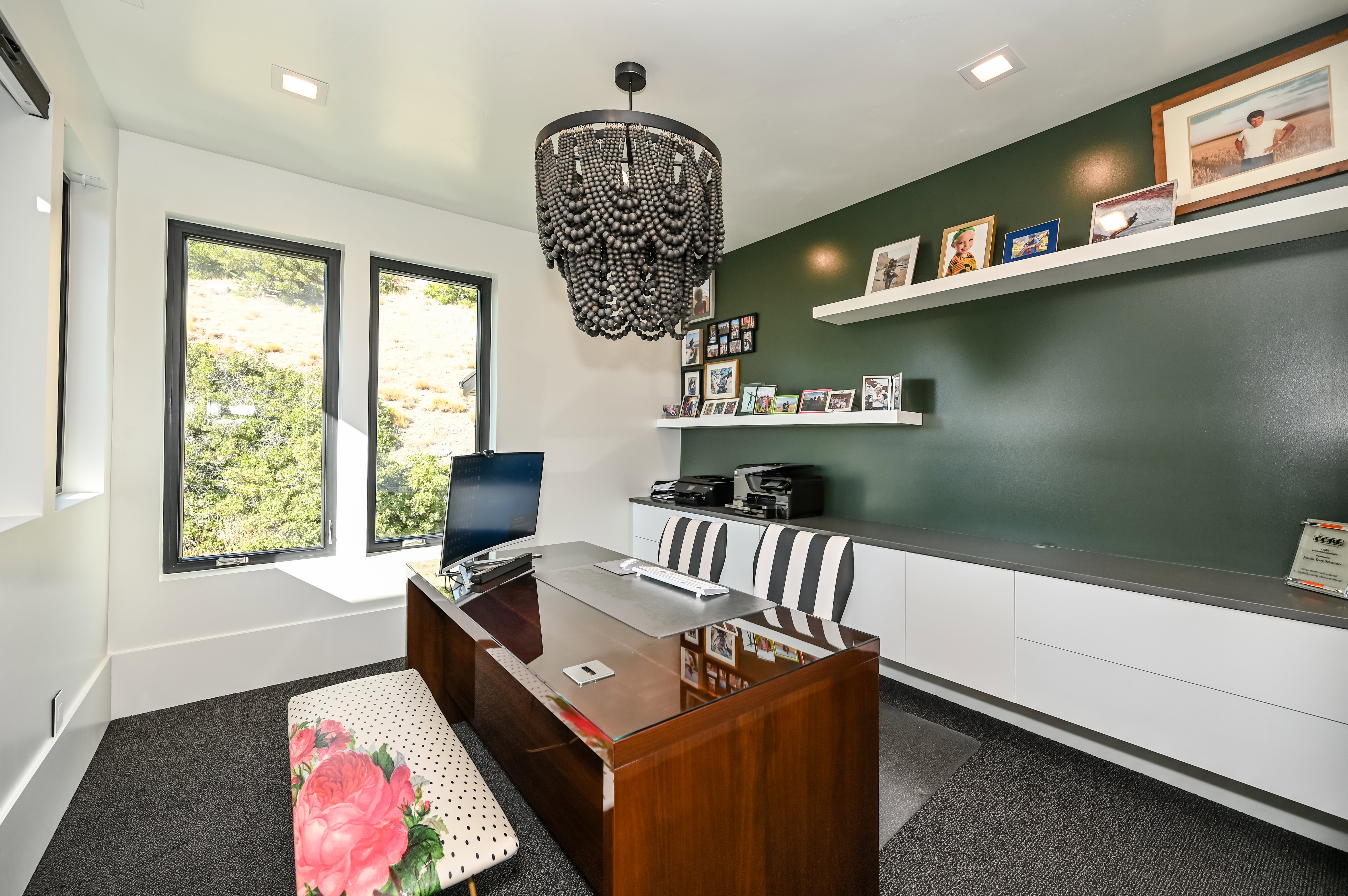 Dedicated workspace featuring a striking beaded chandelier, recessed lighting, and a dark green accent wall with floating shelves