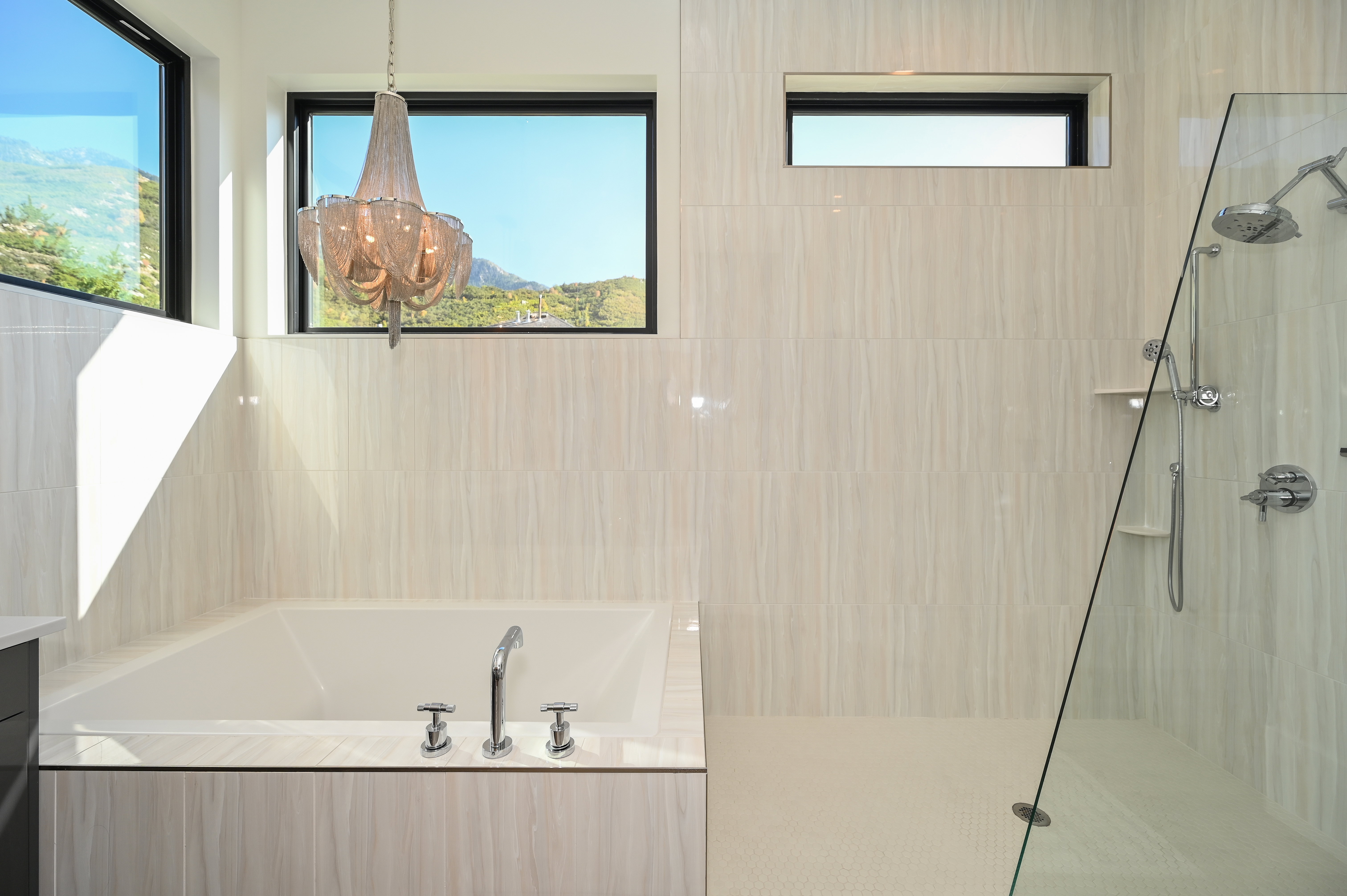 Freestanding soaking tub with polished chrome fixtures, flanked by large windows