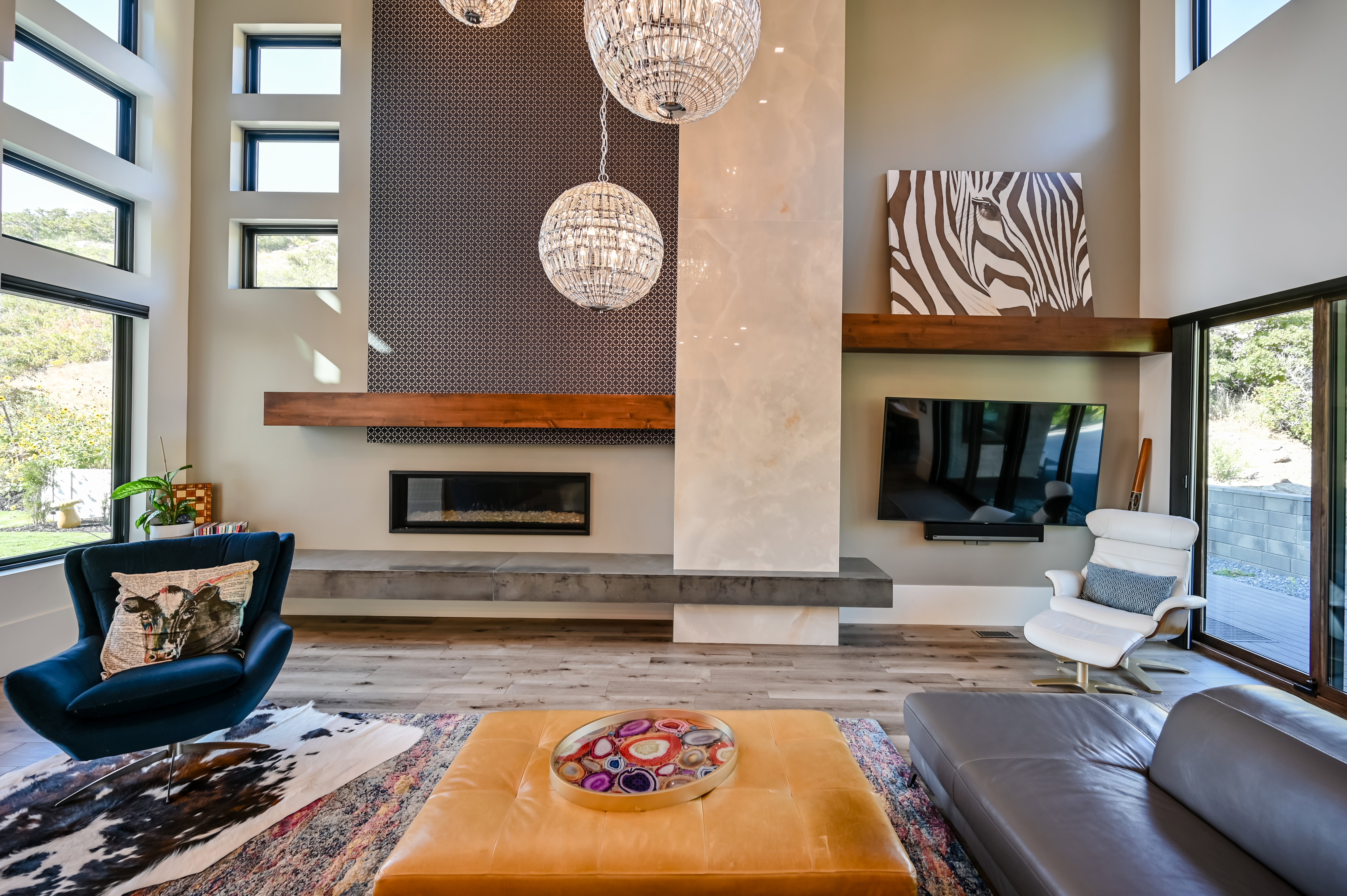 Double-height living space featuring a linear fireplace, decorative patterned wall paneling, a substantial wood mantel, and large picture windows