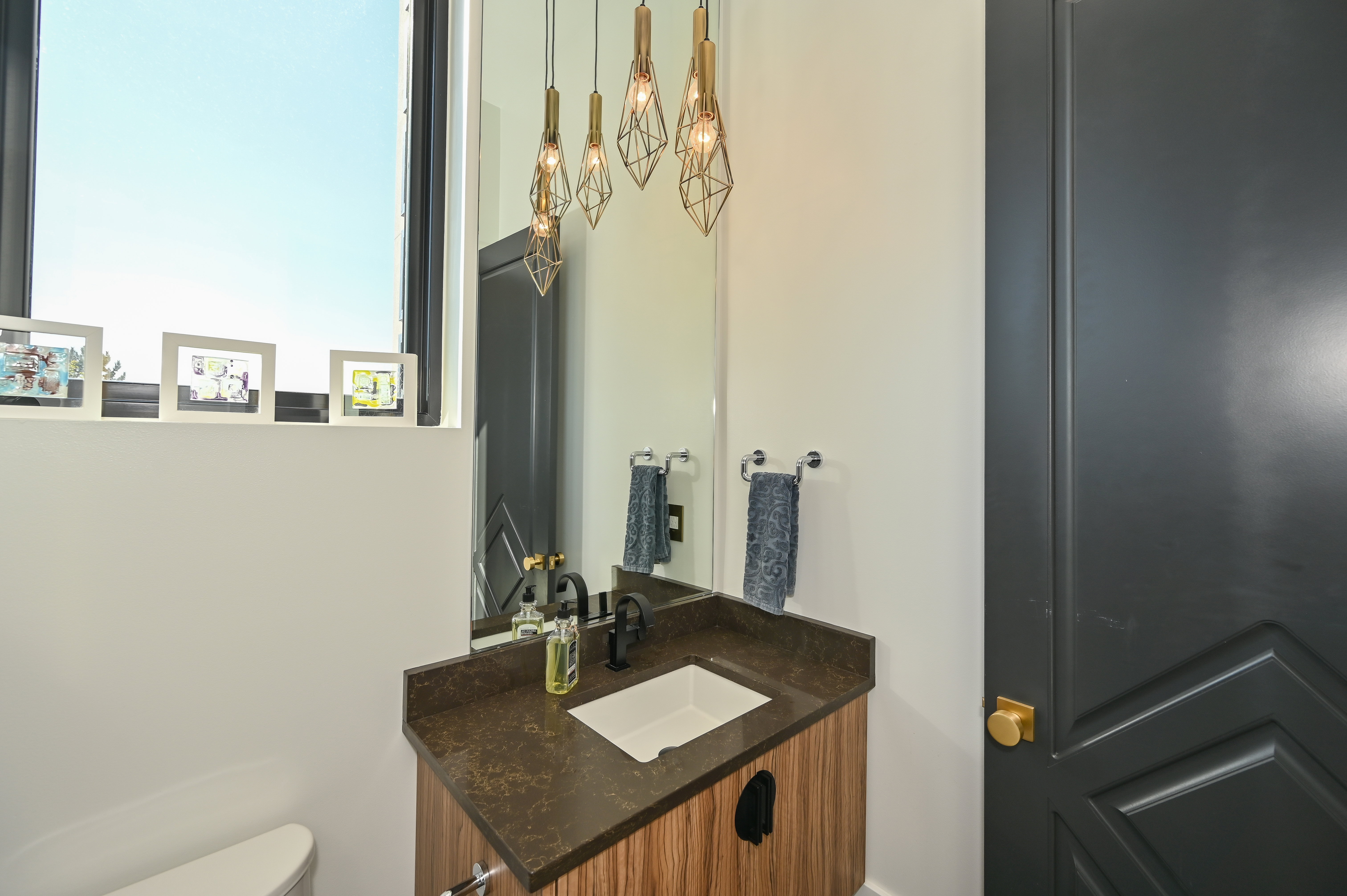 Powder room featuring a wood-finish vanity with an integrated sink, dark countertop, and matte black faucet
