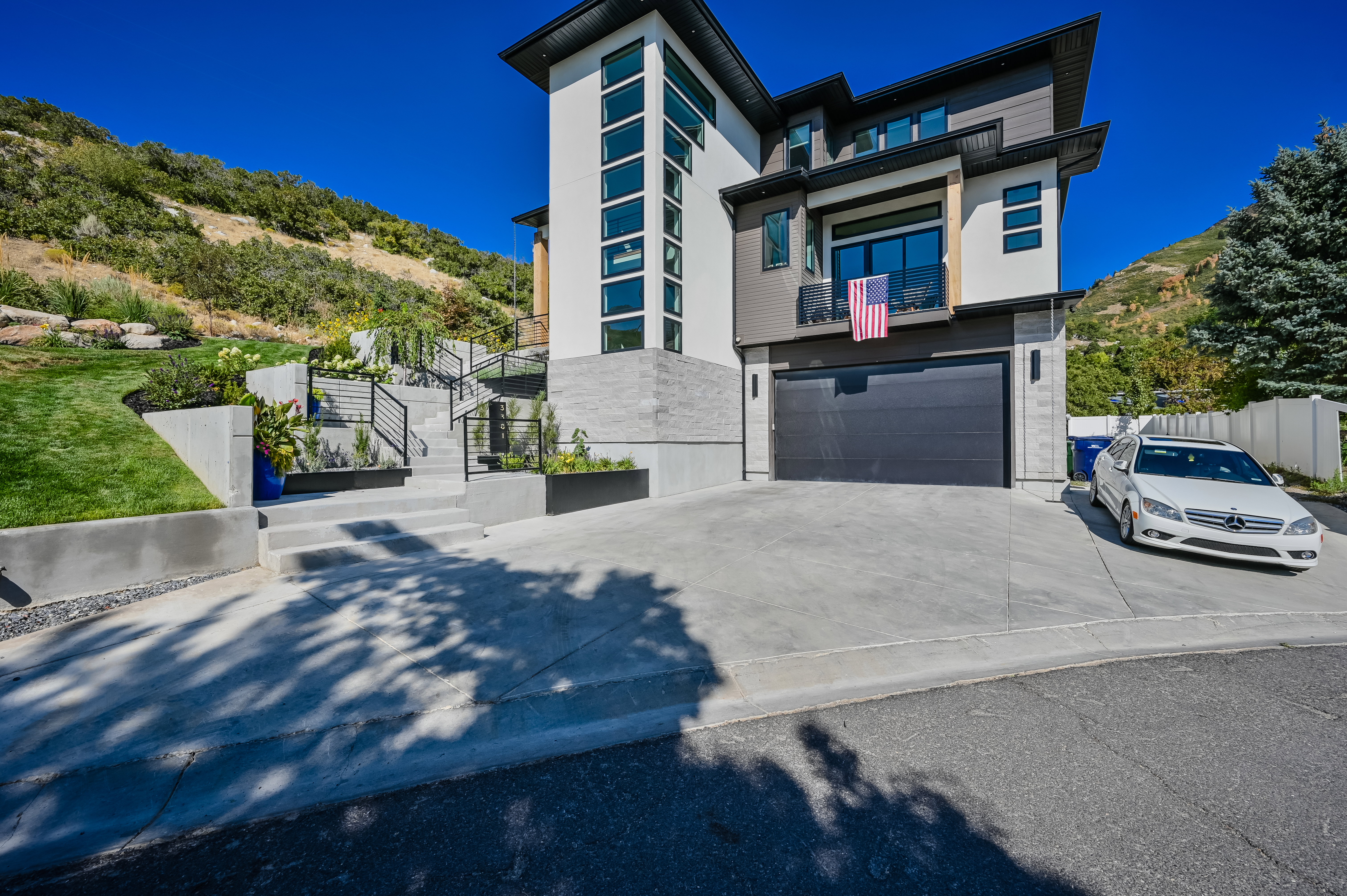 Modern architectural residence featuring a multi-level concrete staircase with black metal railings, a dark gray garage door, and a white and gray exterior facade