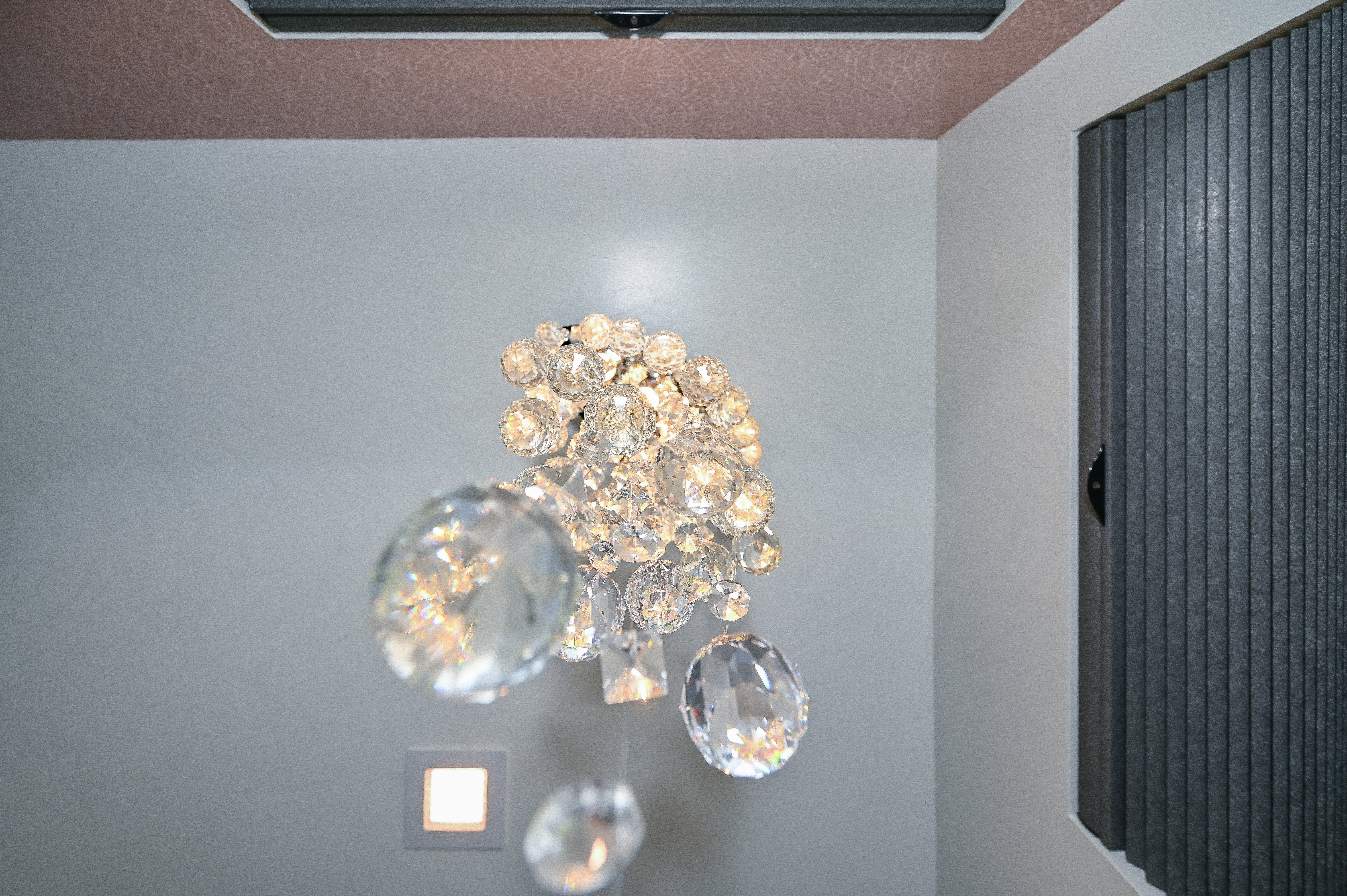 Crystal chandelier with a square recessed light fixture, textured ceiling, and vertical blinds