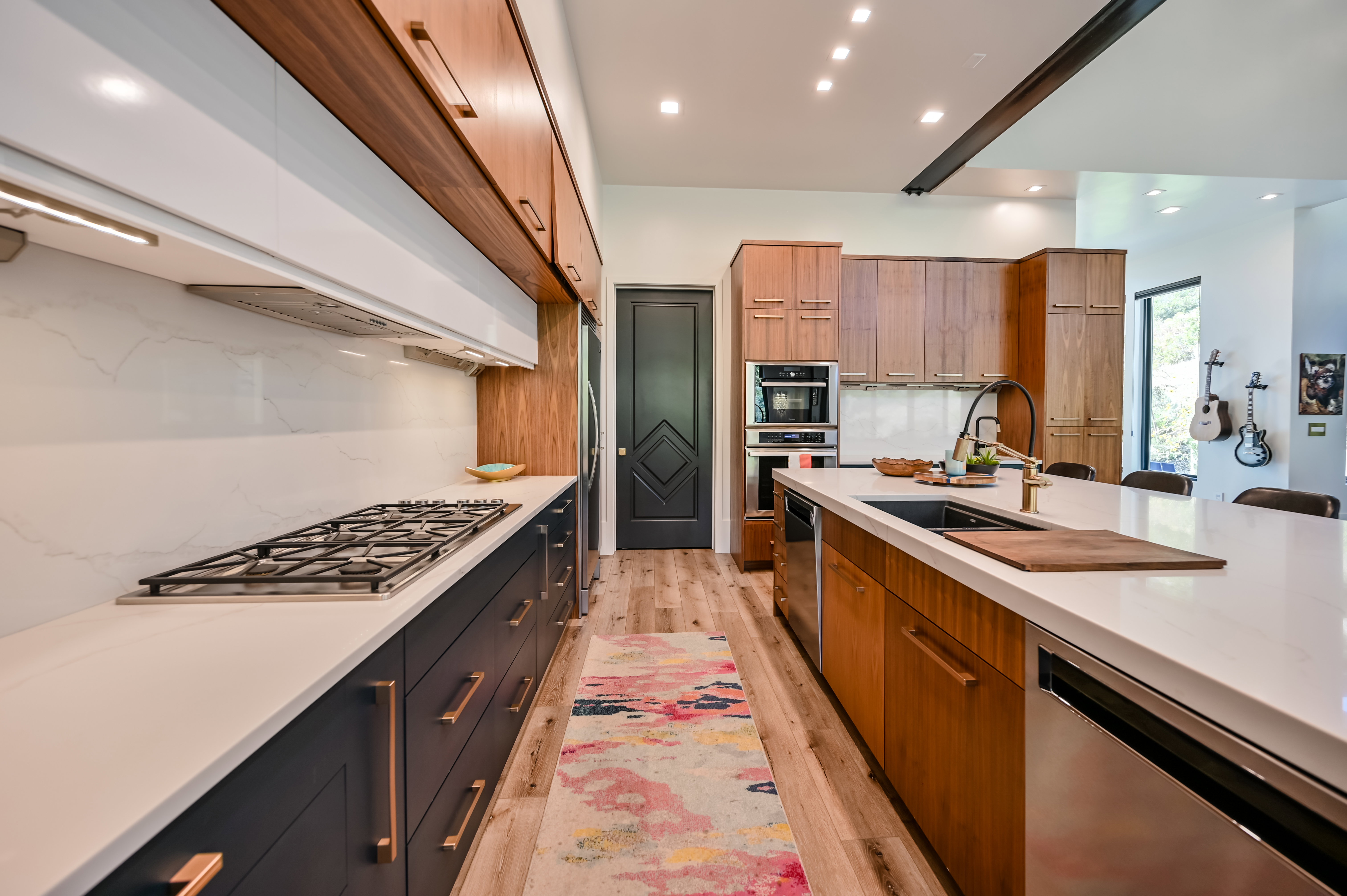 Modern kitchen featuring a gas range, white countertops, built-in stainless steel appliances, a kitchen island with an undermount sink, and wood-finish flooring