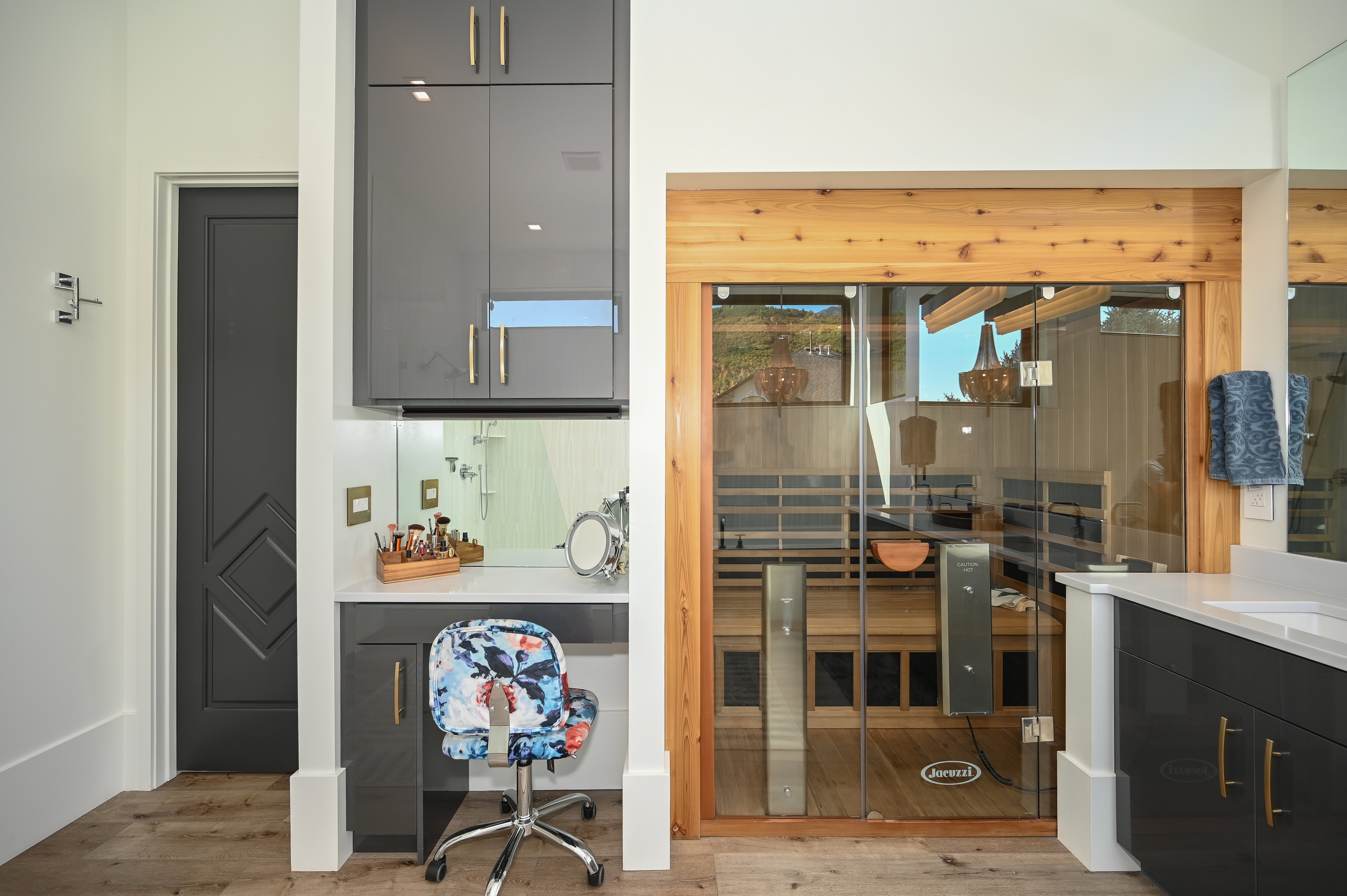 Spa-inspired bathroom featuring a glass-enclosed sauna with cedar framing, integrated vanity with quartz countertop, gloss gray cabinetry with brass-finish hardware, and wood-finish flooring