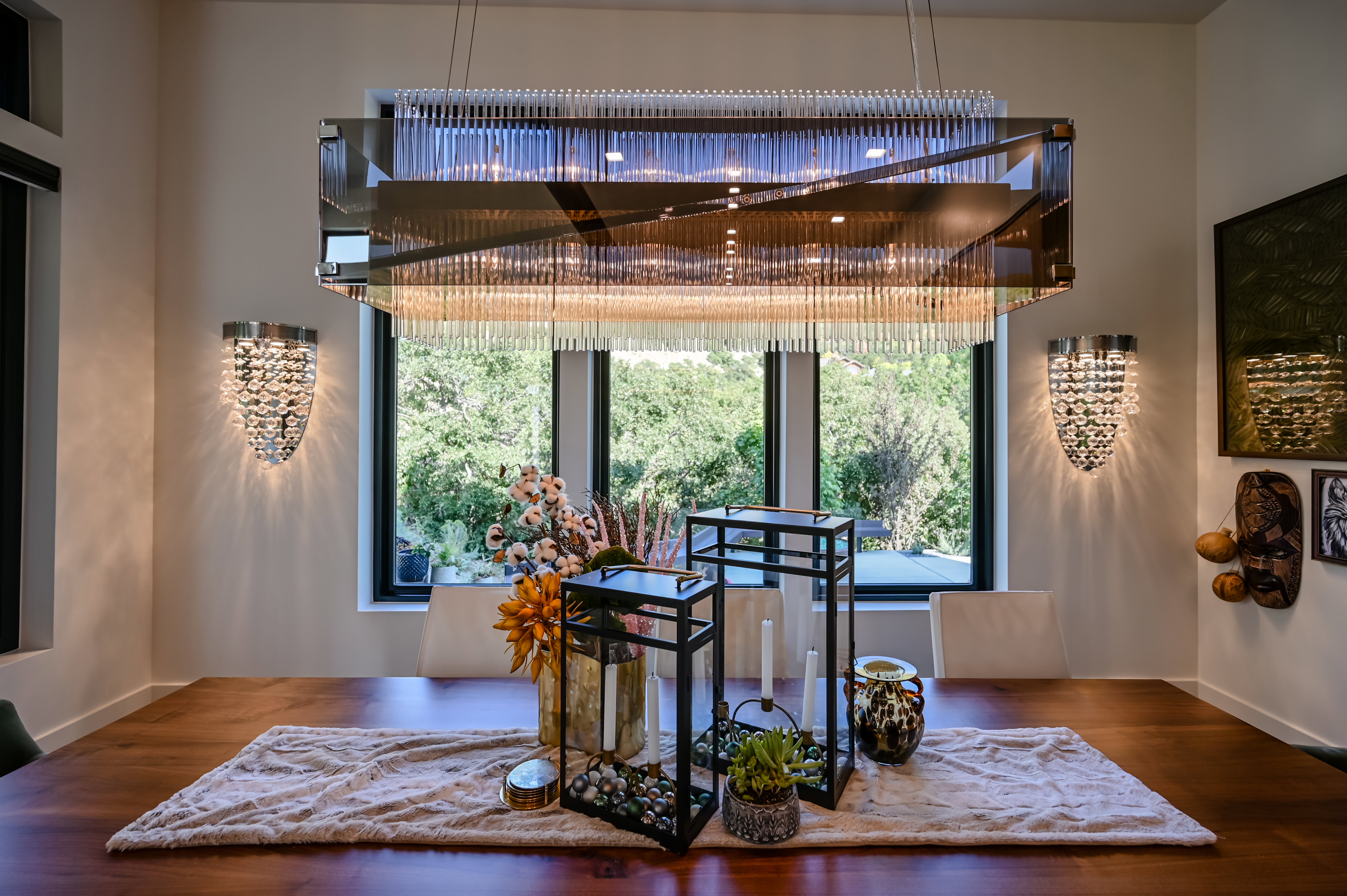 Dining area featuring a rectangular chandelier with clear glass rods, two crystal-style sconces, and a dark wood-finish table