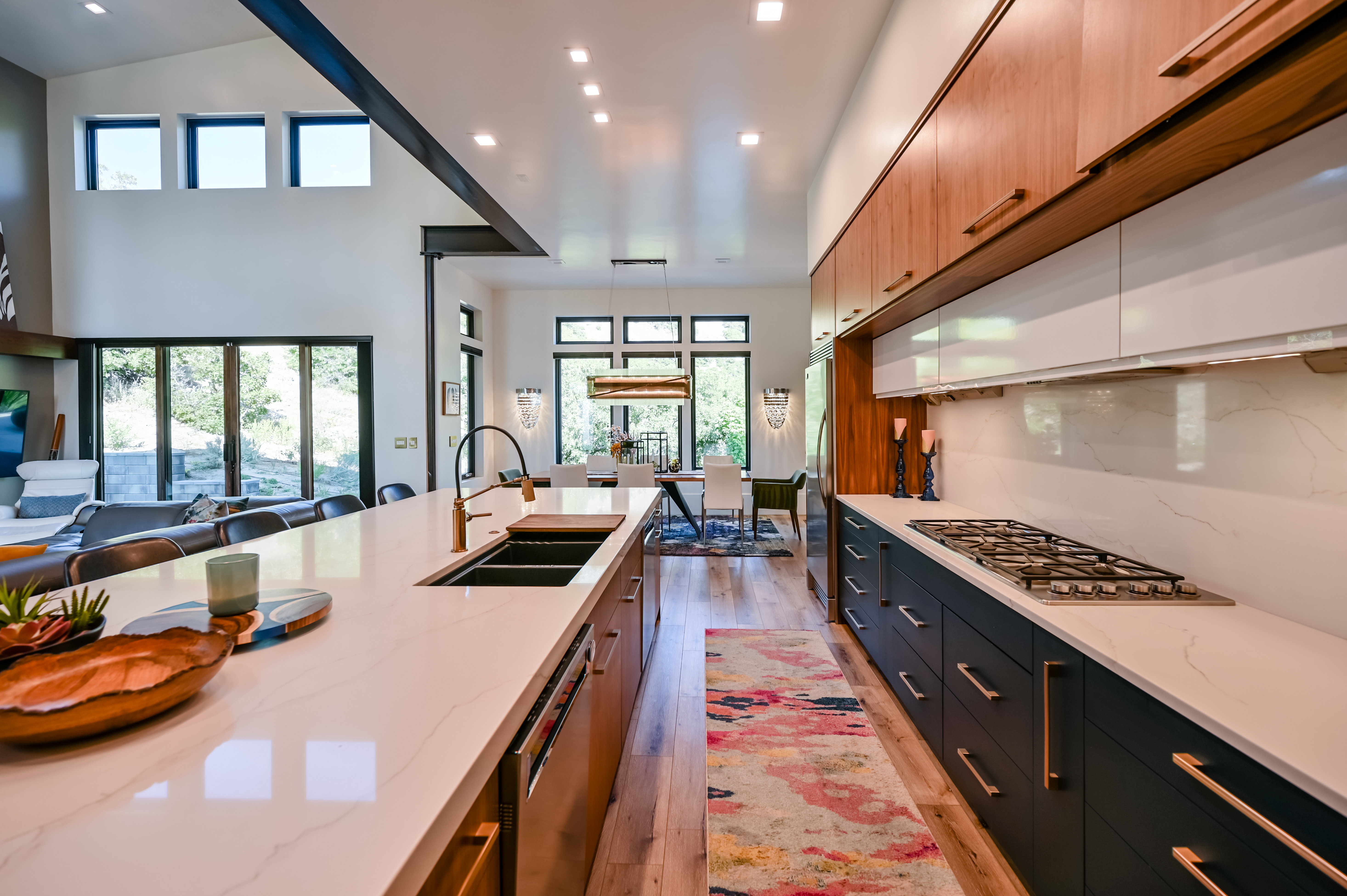 Spacious open-concept kitchen featuring a large island with an integrated sink, quartz countertops, wood-finish flooring, a built-in gas cooktop, and abundant cabinetry