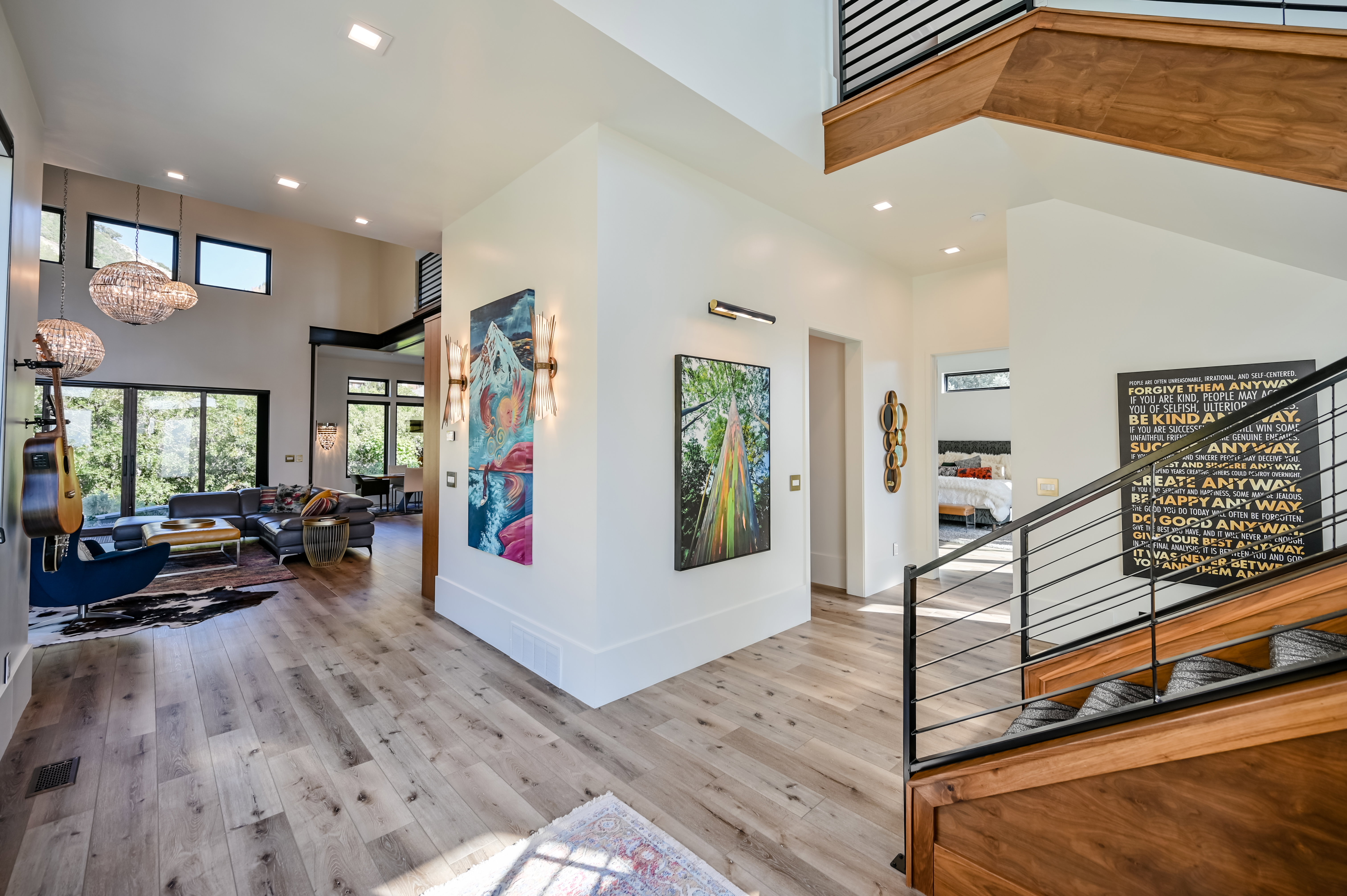 Expansive living area featuring light wood-finish flooring, a contemporary staircase with wood and metal railings, high ceilings, large windows, and recessed lighting